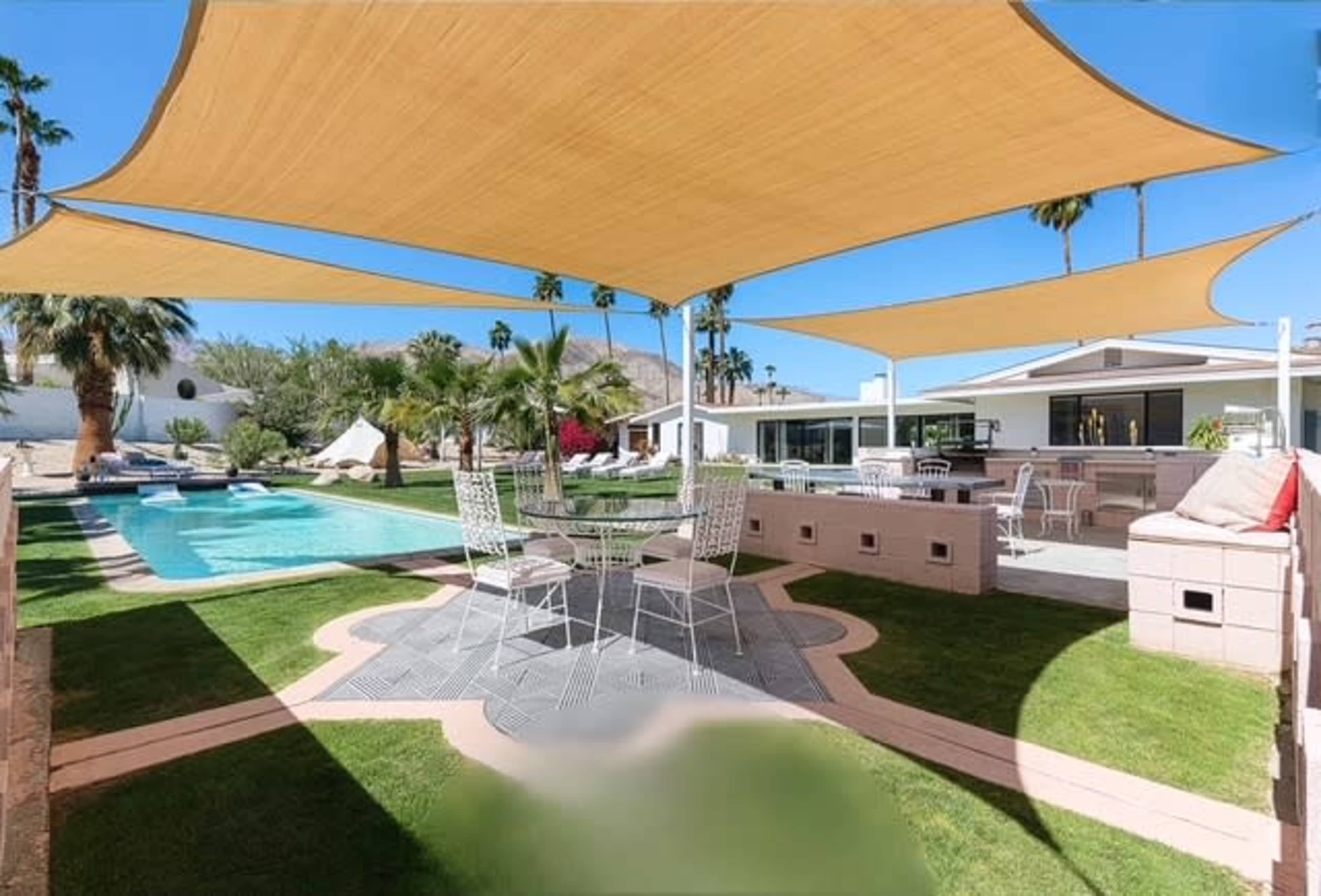 The image shows a landscaped backyard with a swimming pool, shaded seating area, and modern outdoor furniture.