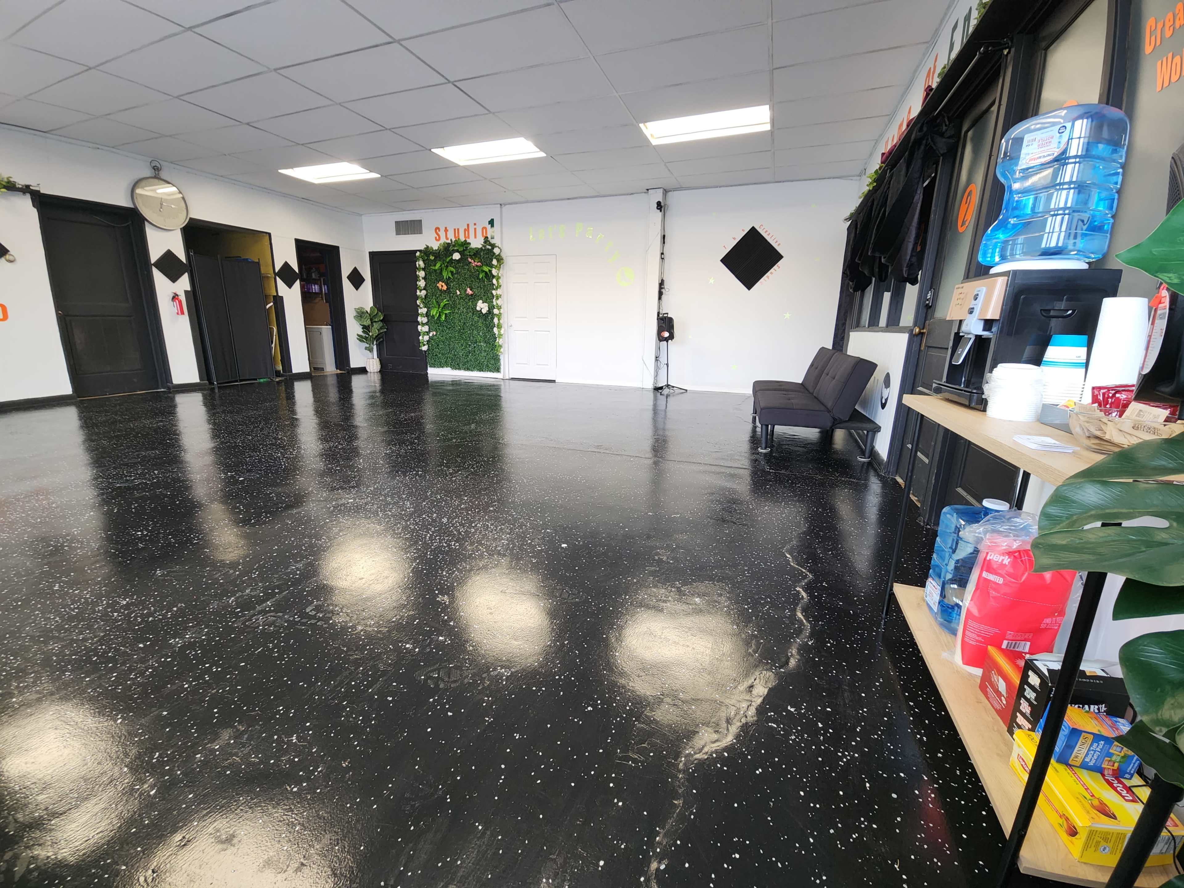An empty room with a polished black floor, a few plants on the walls, and a beverage station on the right side.