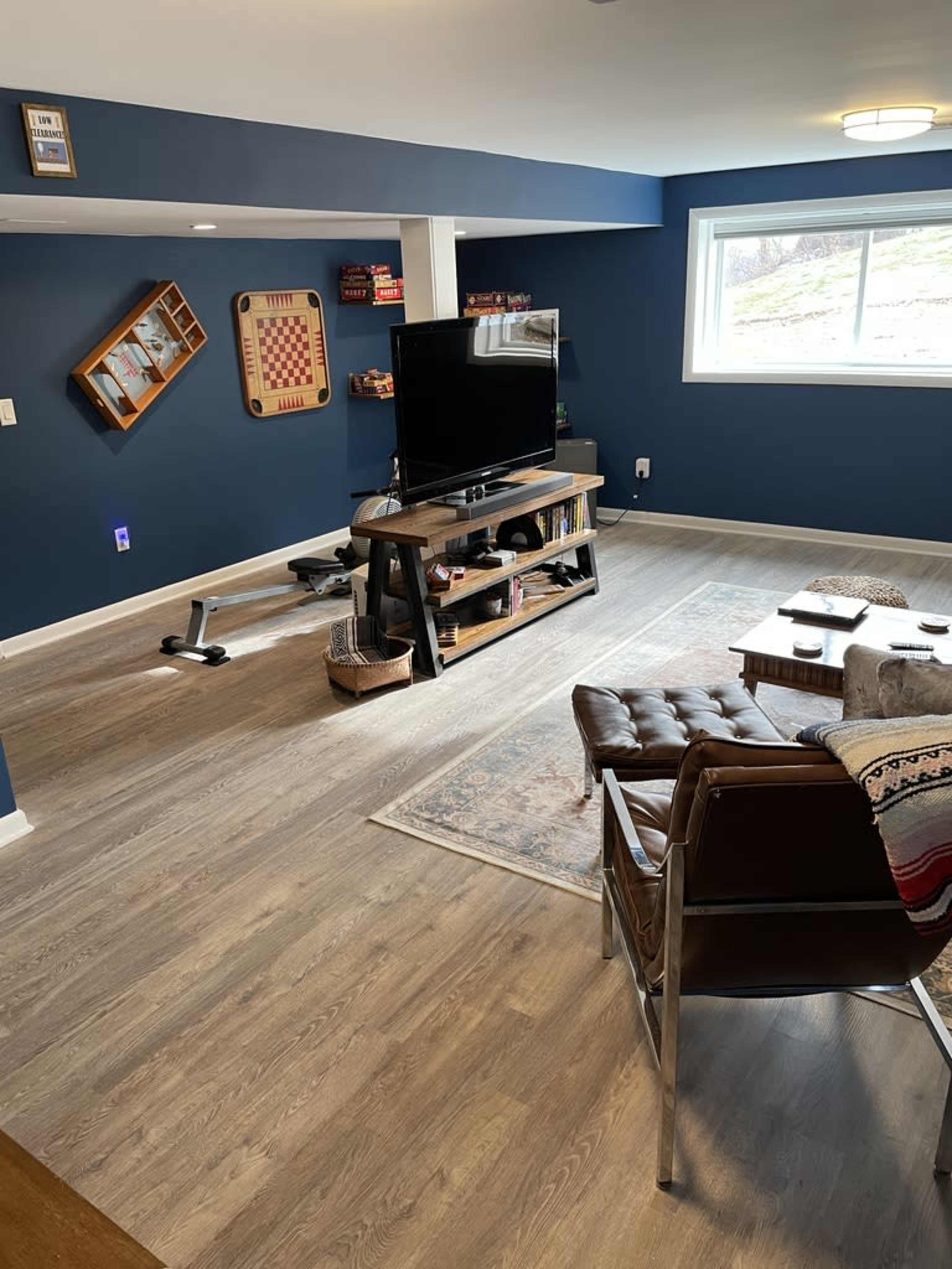 A modern basement living area with a television mounted on the wall, a brown leather chair, a shelf with books, and a game board on display.