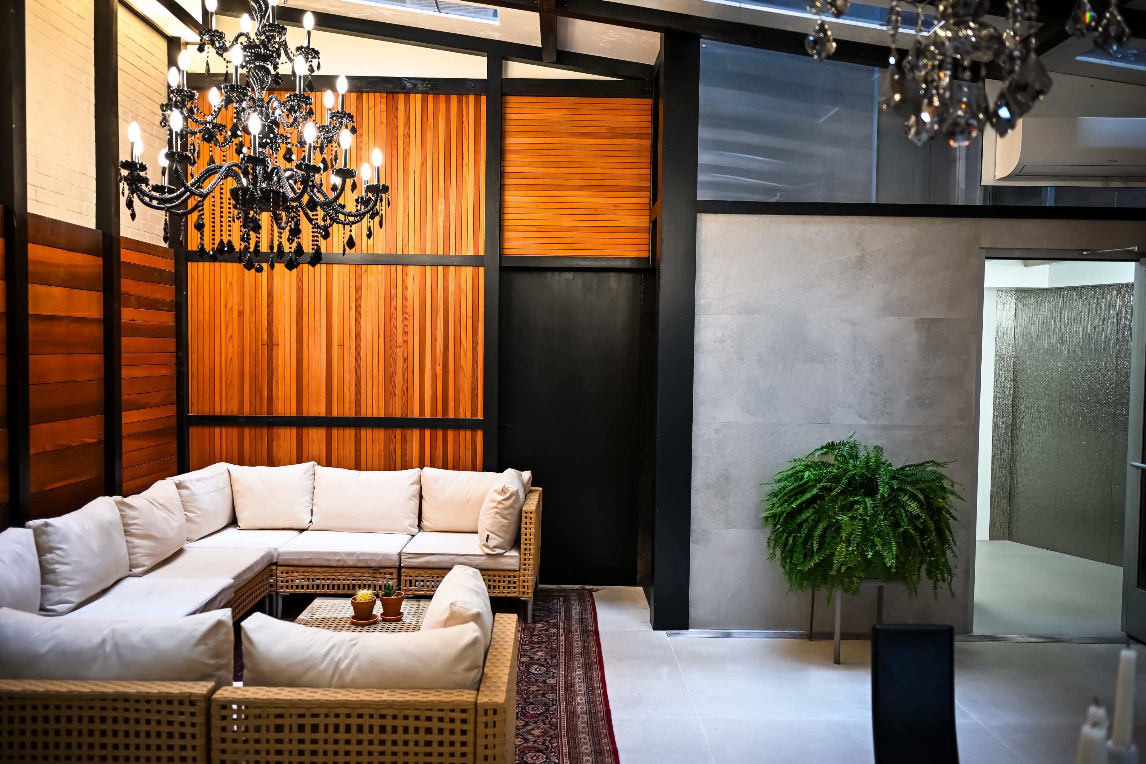 The image features a contemporary indoor lounge area with a large sectional sofa, a chandelier, wooden paneling, and a potted plant in the corner.