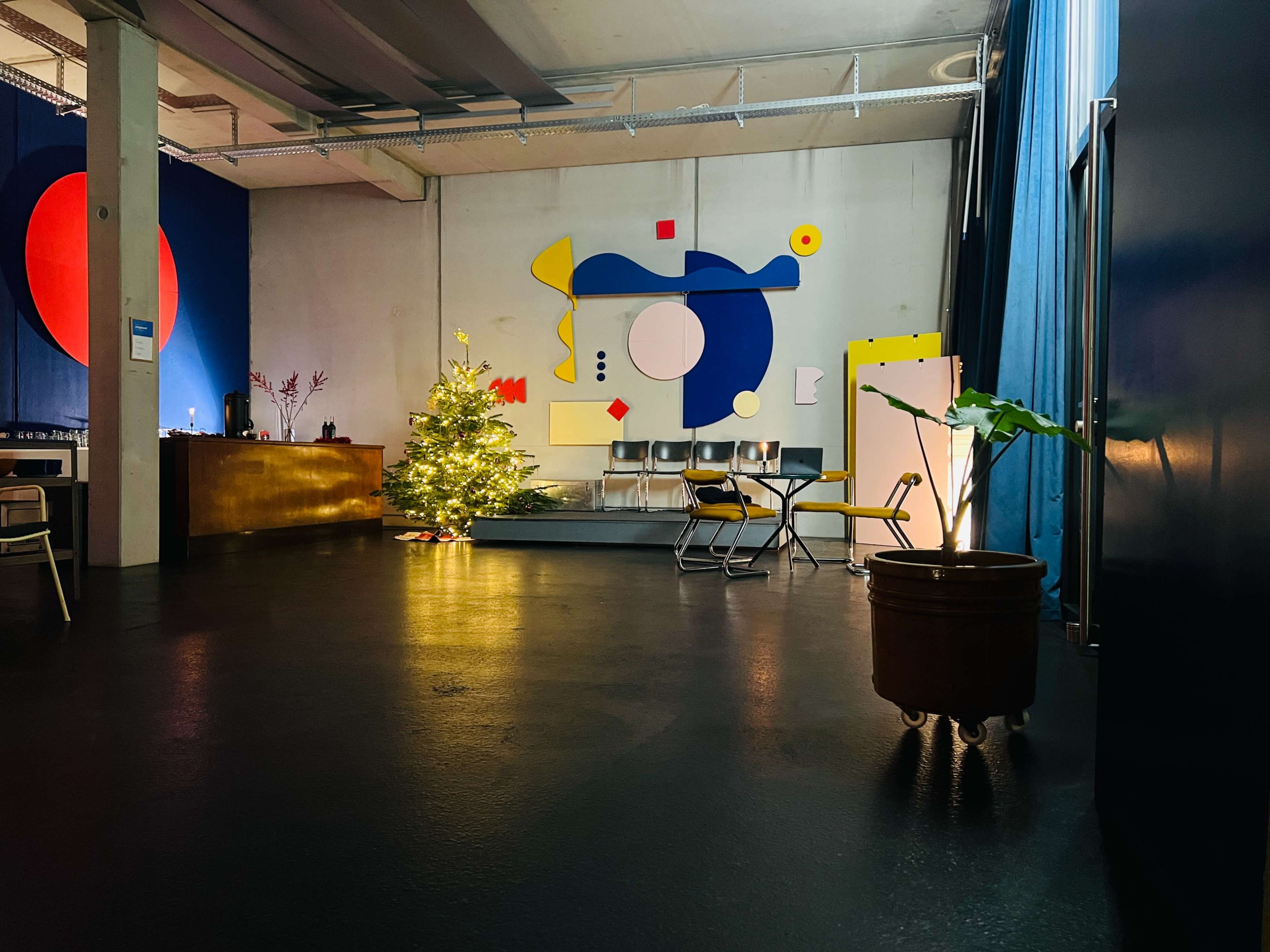 An interior space featuring a decorative Christmas tree, modern artworks on the walls, and a few chairs arranged in the room.