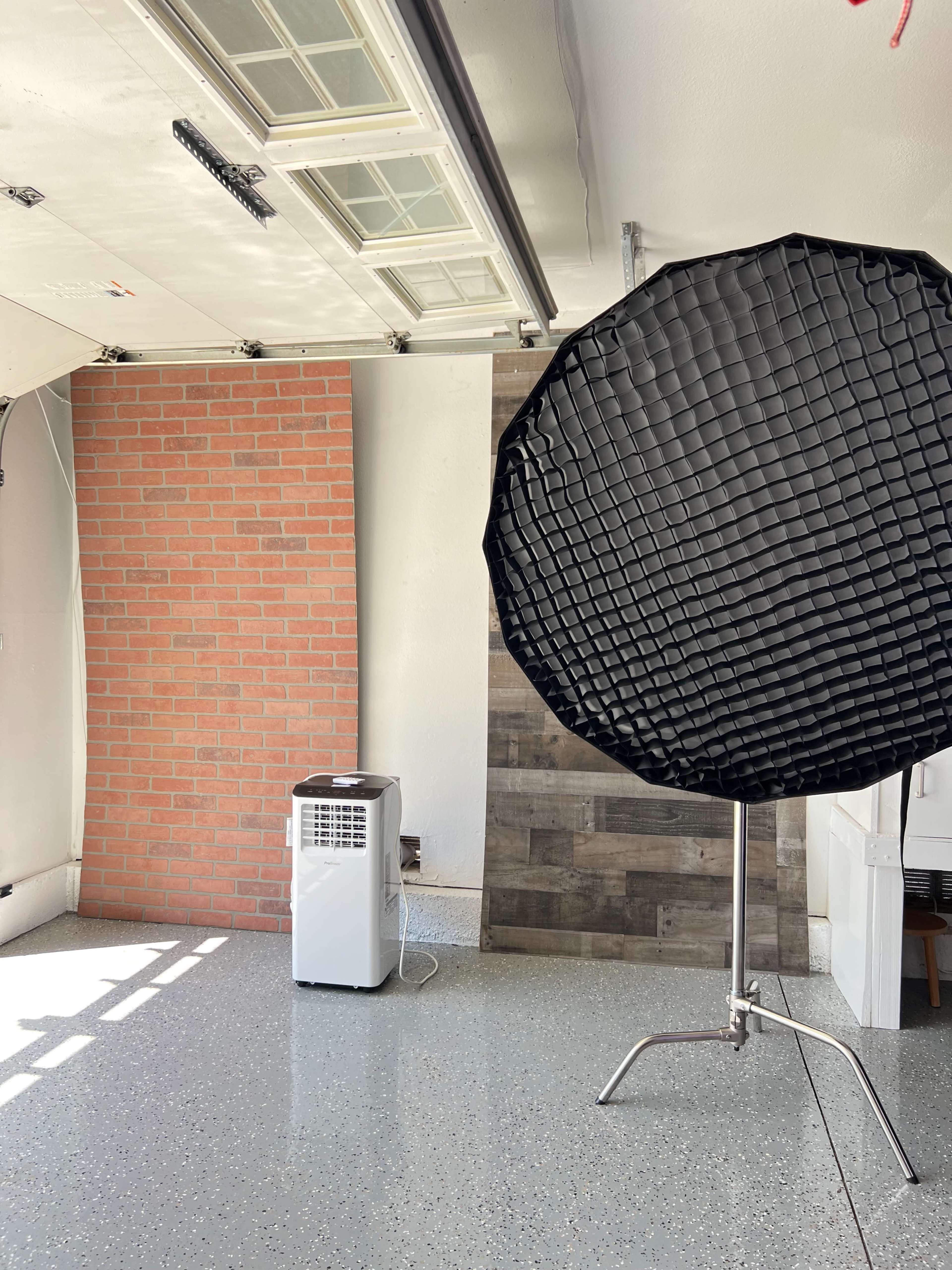 A garage interior featuring a brick wall, a wooden panel wall, an air conditioner, and a large softbox light on a stand.