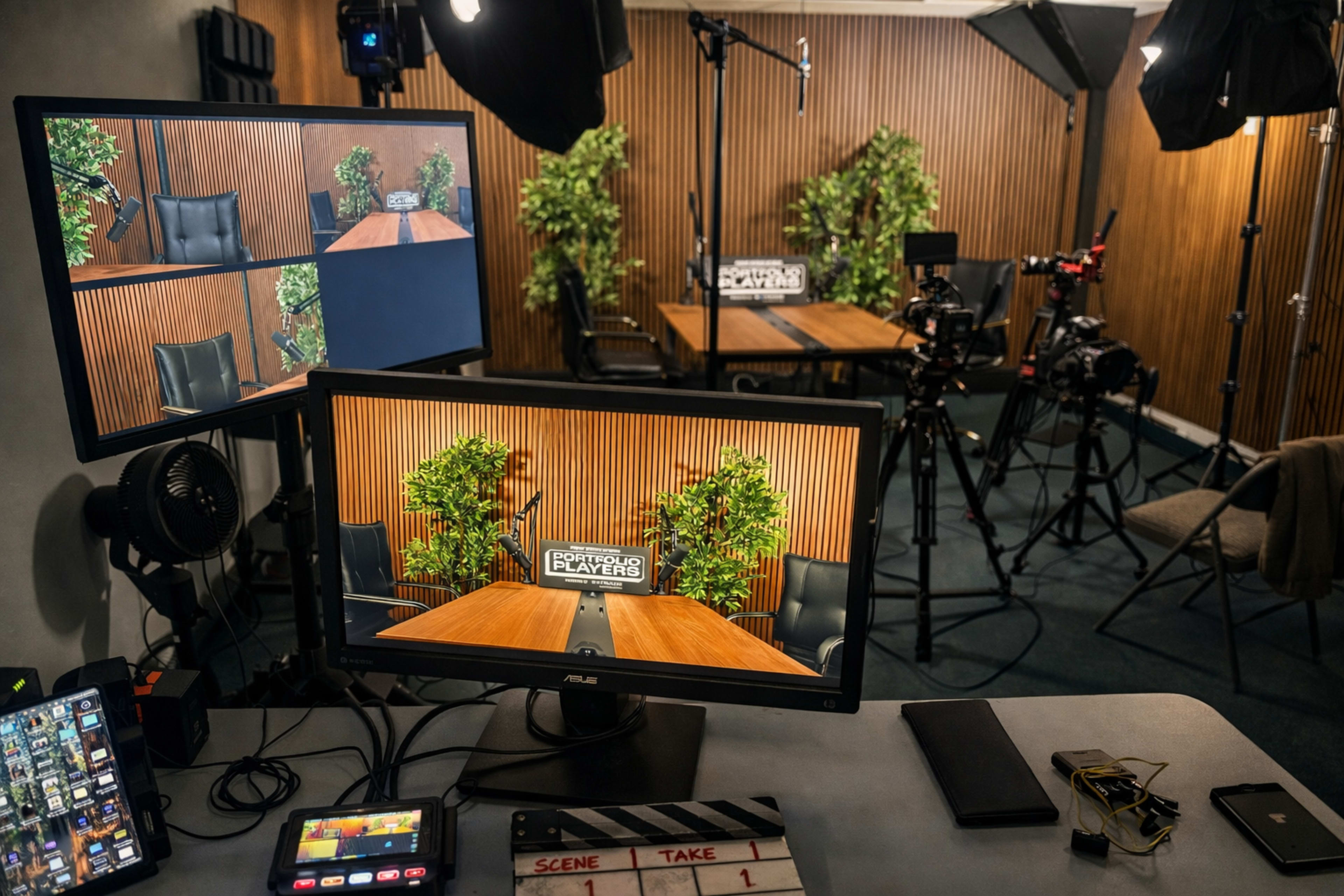 The image shows a video production setup featuring multiple screens displaying a conference room with a wooden backdrop, surrounded by cameras and lighting equipment.