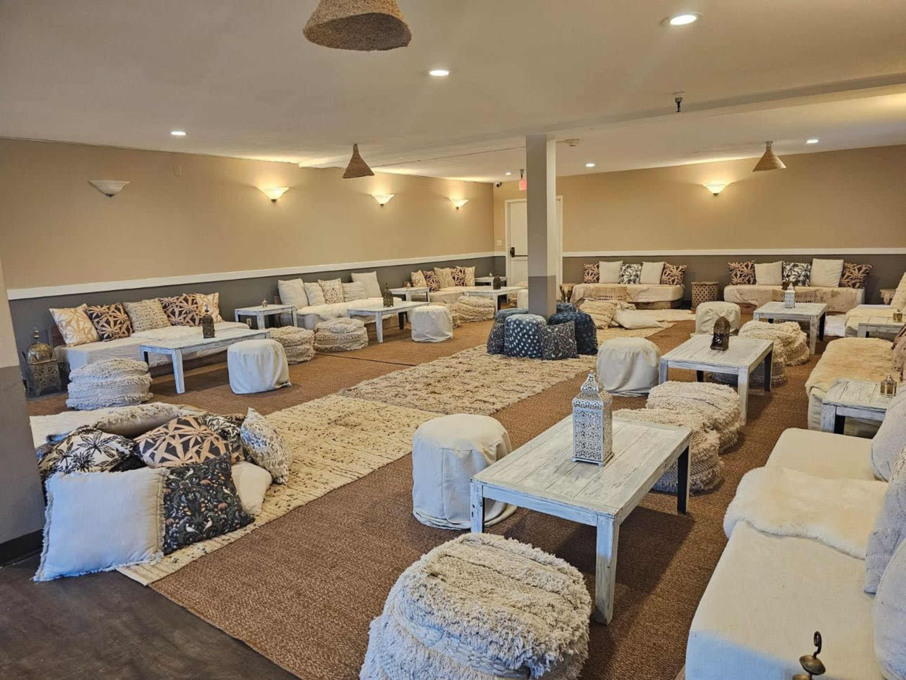 The image shows a spacious lounge area with low seating, rugs, and decorative cushions arranged in a symmetrical layout.