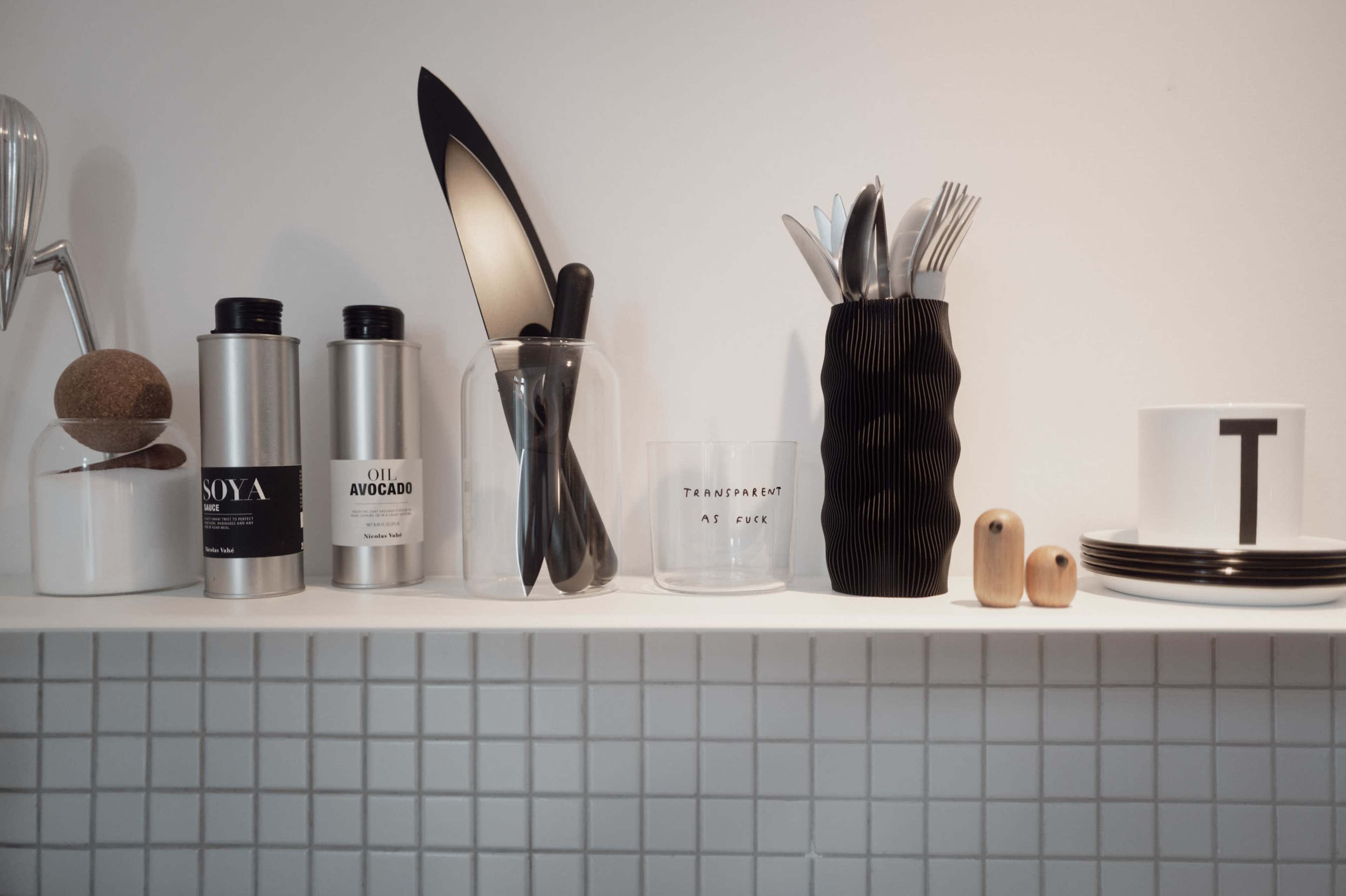 The image displays a clean kitchen shelf containing various kitchen tools, including knives, containers, utensils, and a decorative cup.