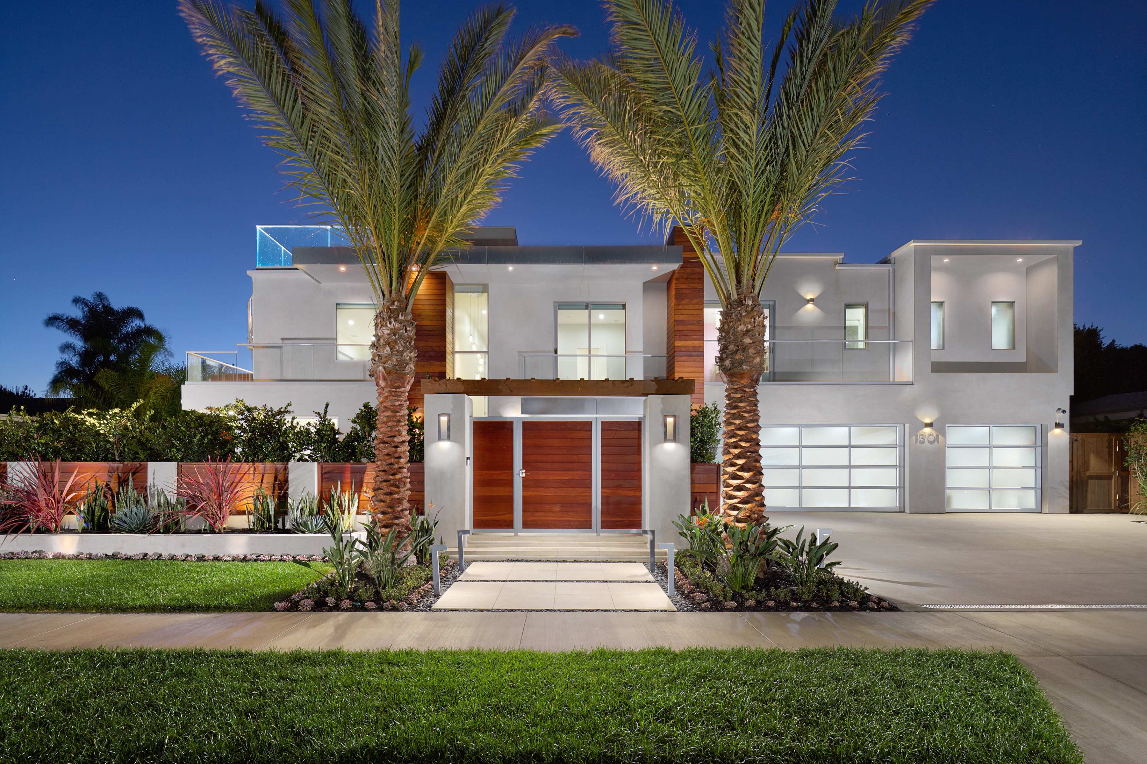 A modern two-story house with palm trees in front, featuring large windows and a wooden entryway.