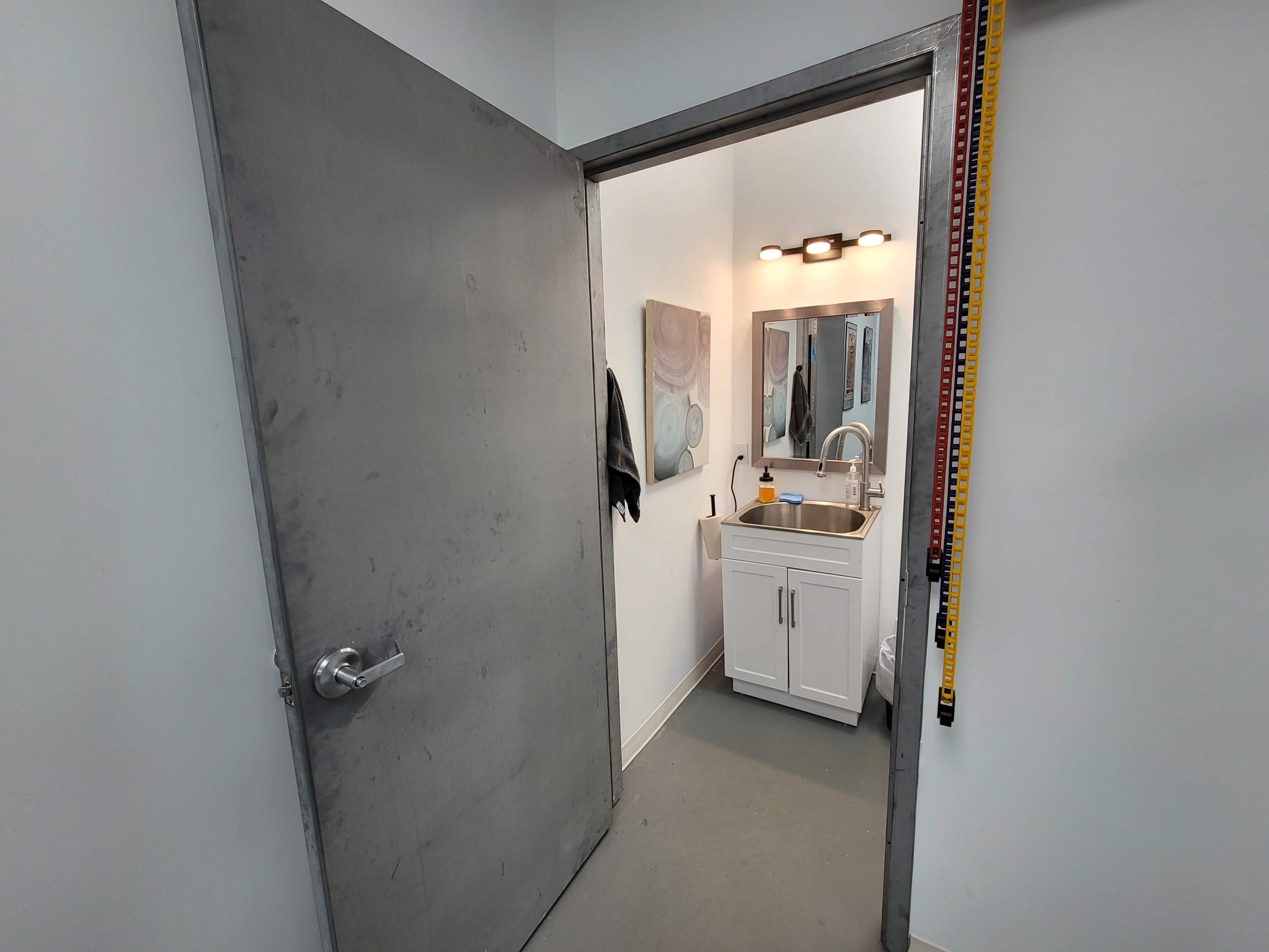 The image shows a bathroom doorway leading to a small, well-lit space with a sink, mirror, and minimal decorations.