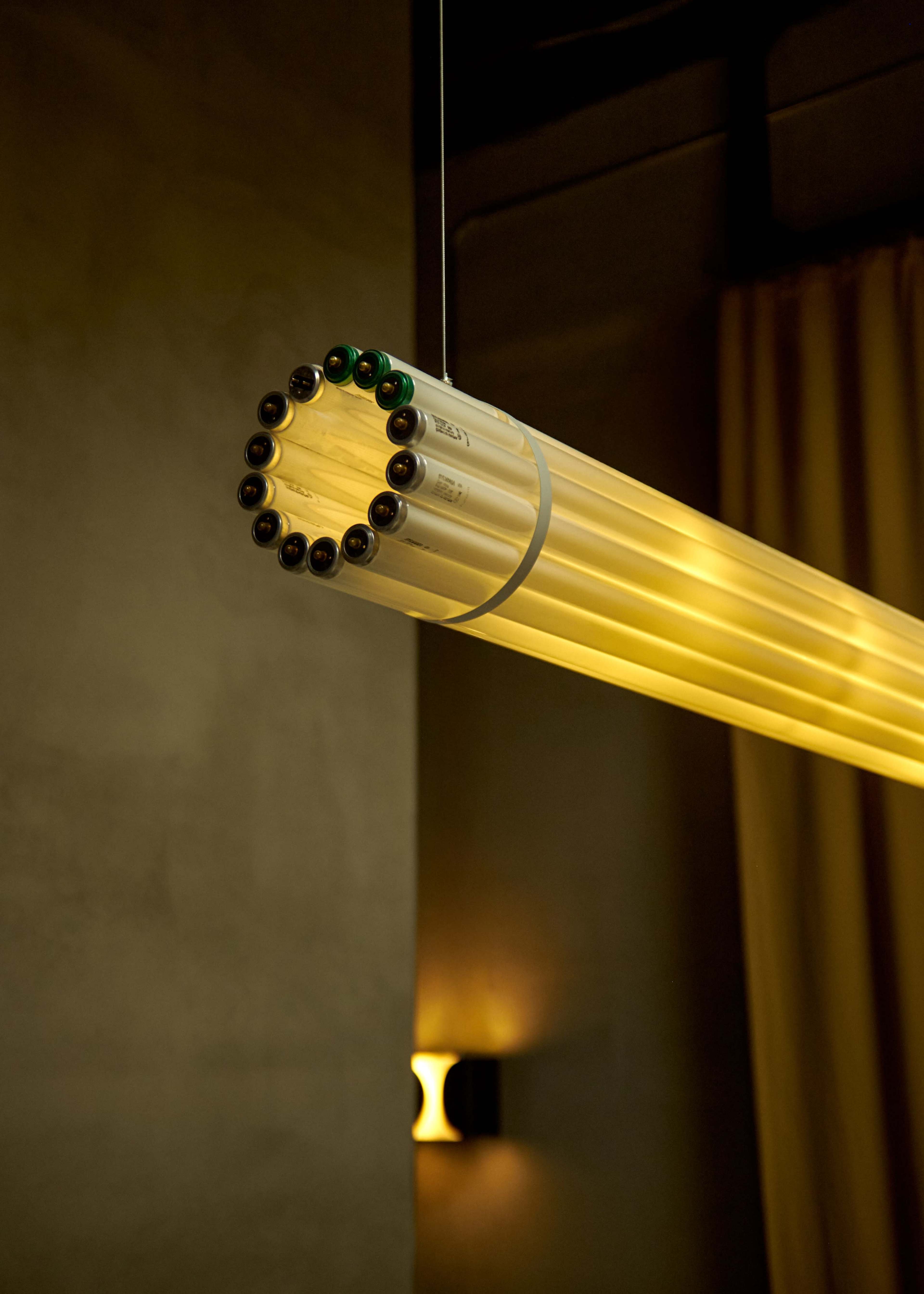 A circular light fixture composed of fluorescent tubes hangs from the ceiling against a dimly lit wall.