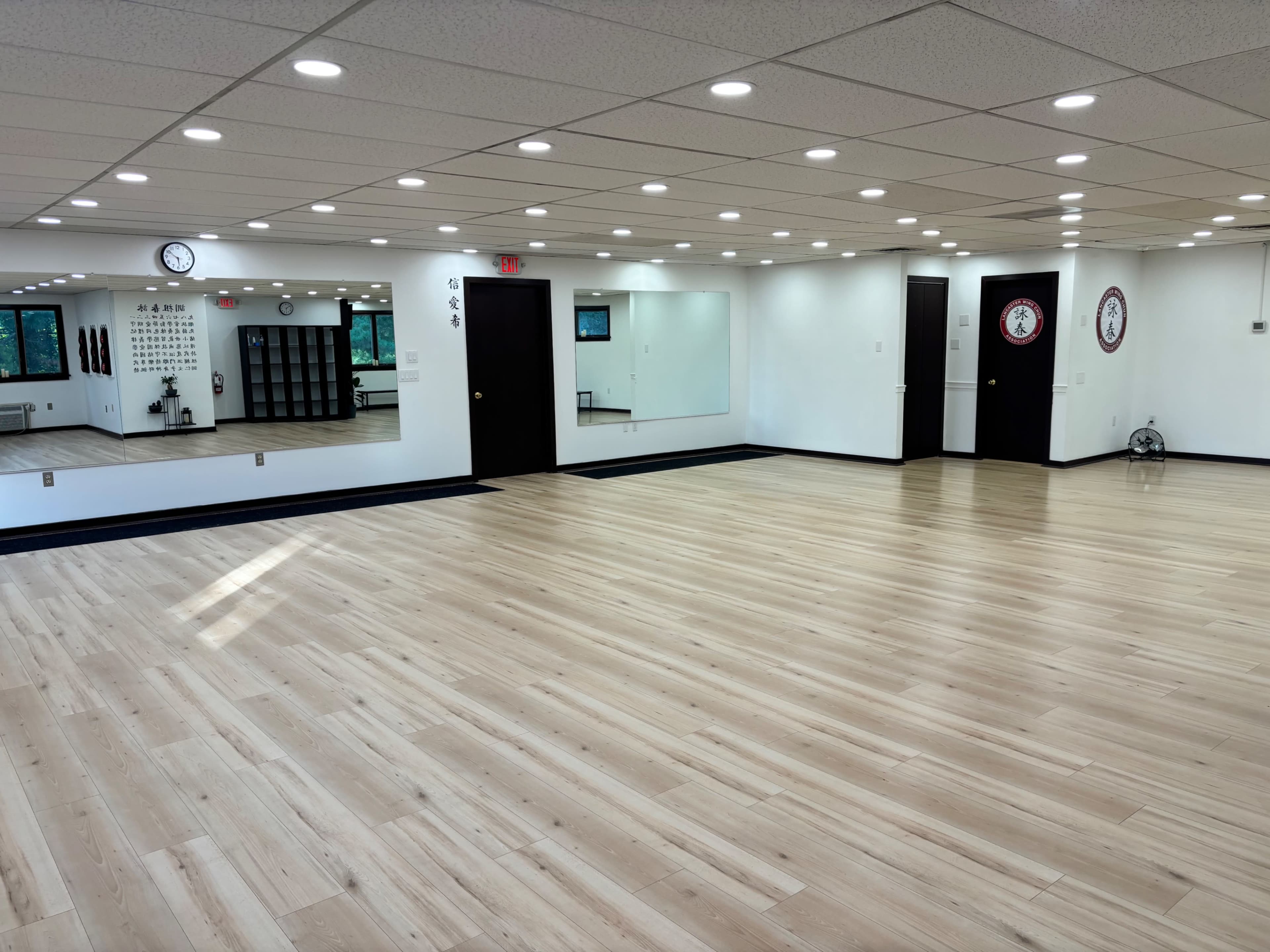 The image shows a spacious, well-lit indoor studio with wooden flooring and large mirrors on the walls.