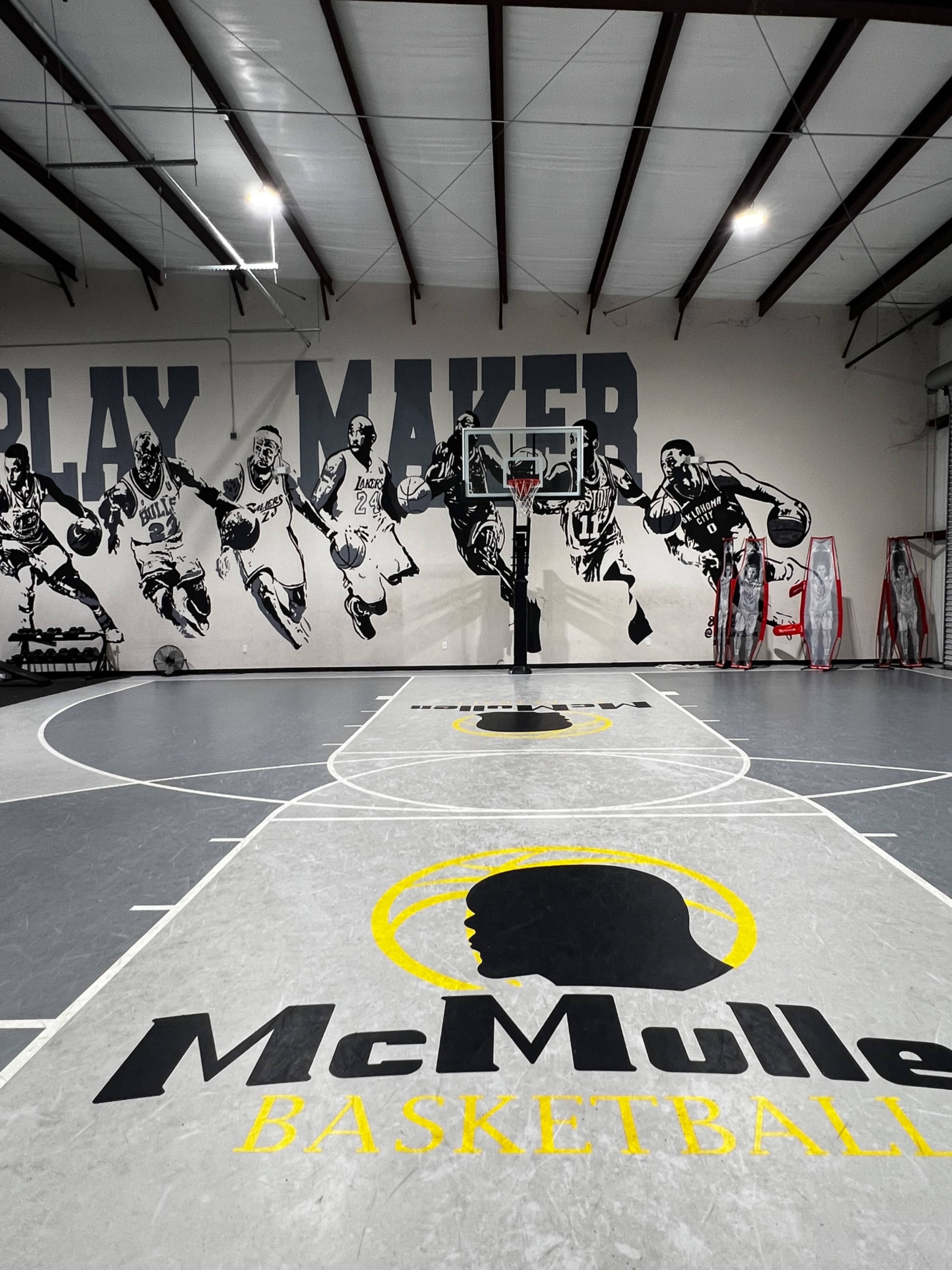 The image shows a basketball court featuring a mural of players on the wall and a central hoop with "McMullen BASKETBALL" printed on the floor.