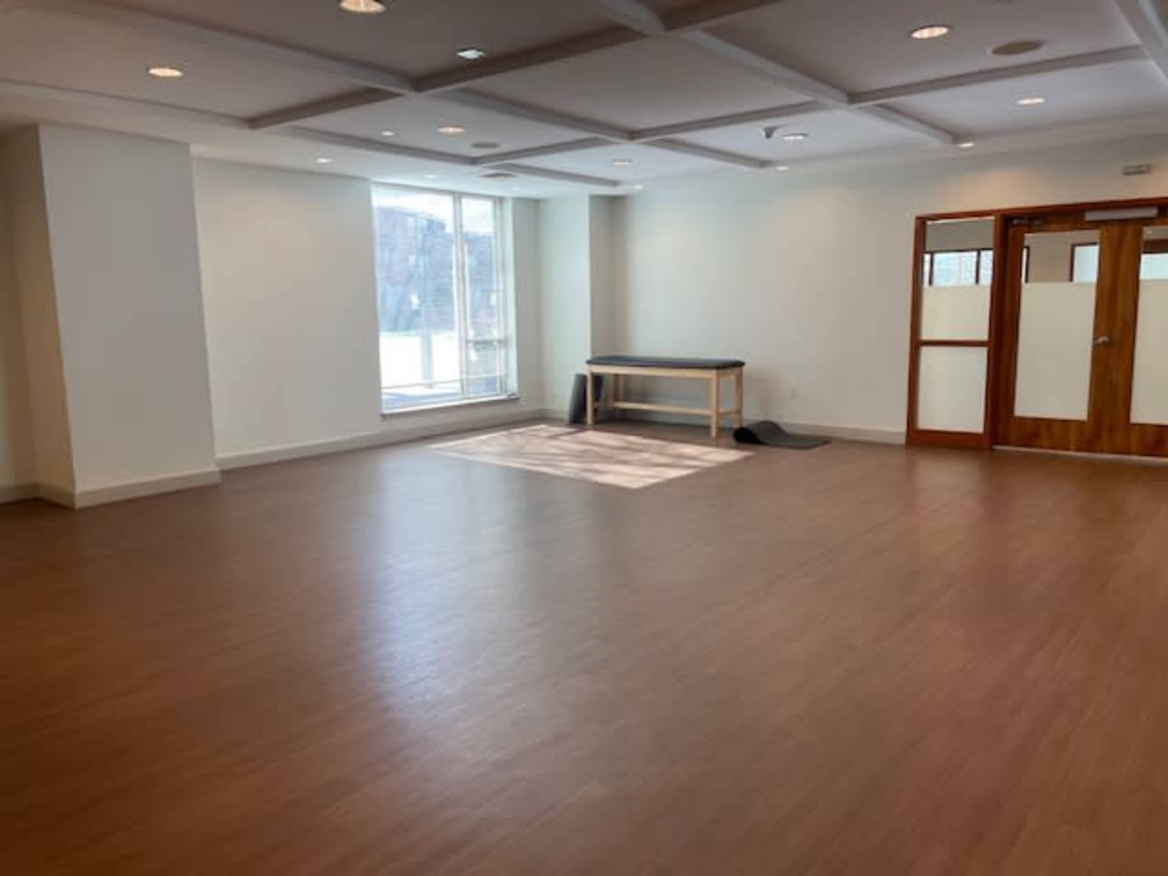 The image shows a spacious, empty room with a large window and a table against one wall.