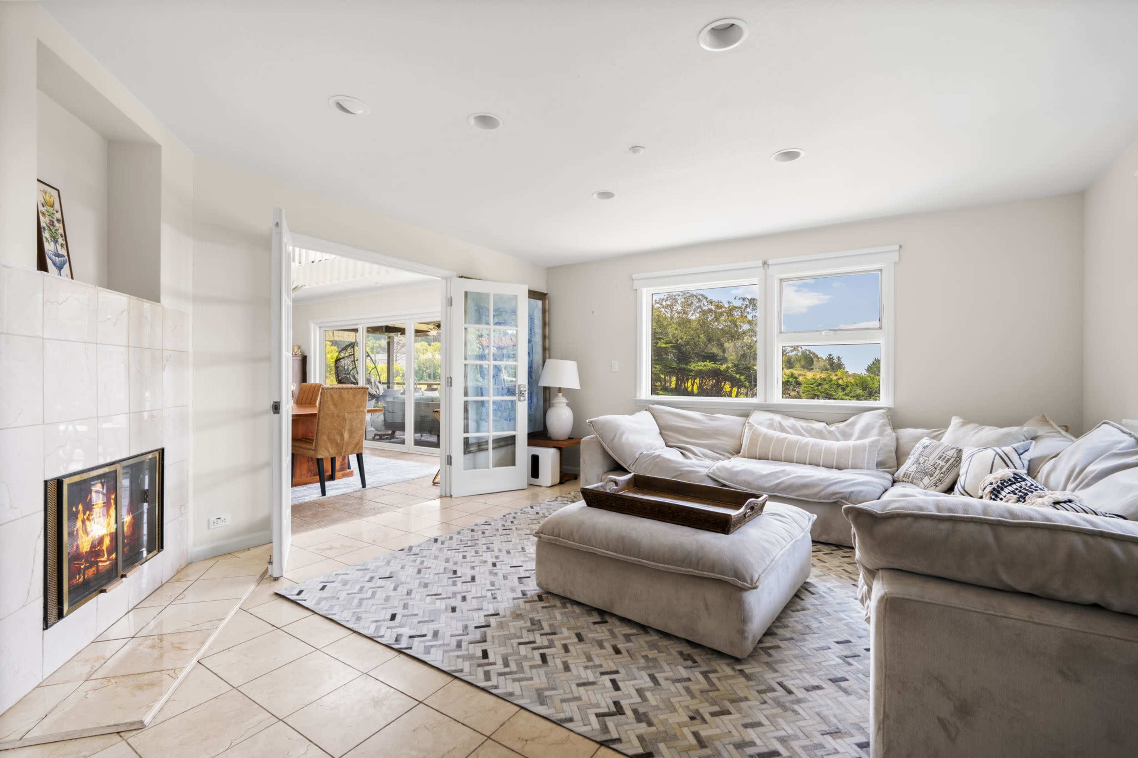A cozy living room features a fireplace, large windows, and a view of an outdoor space.