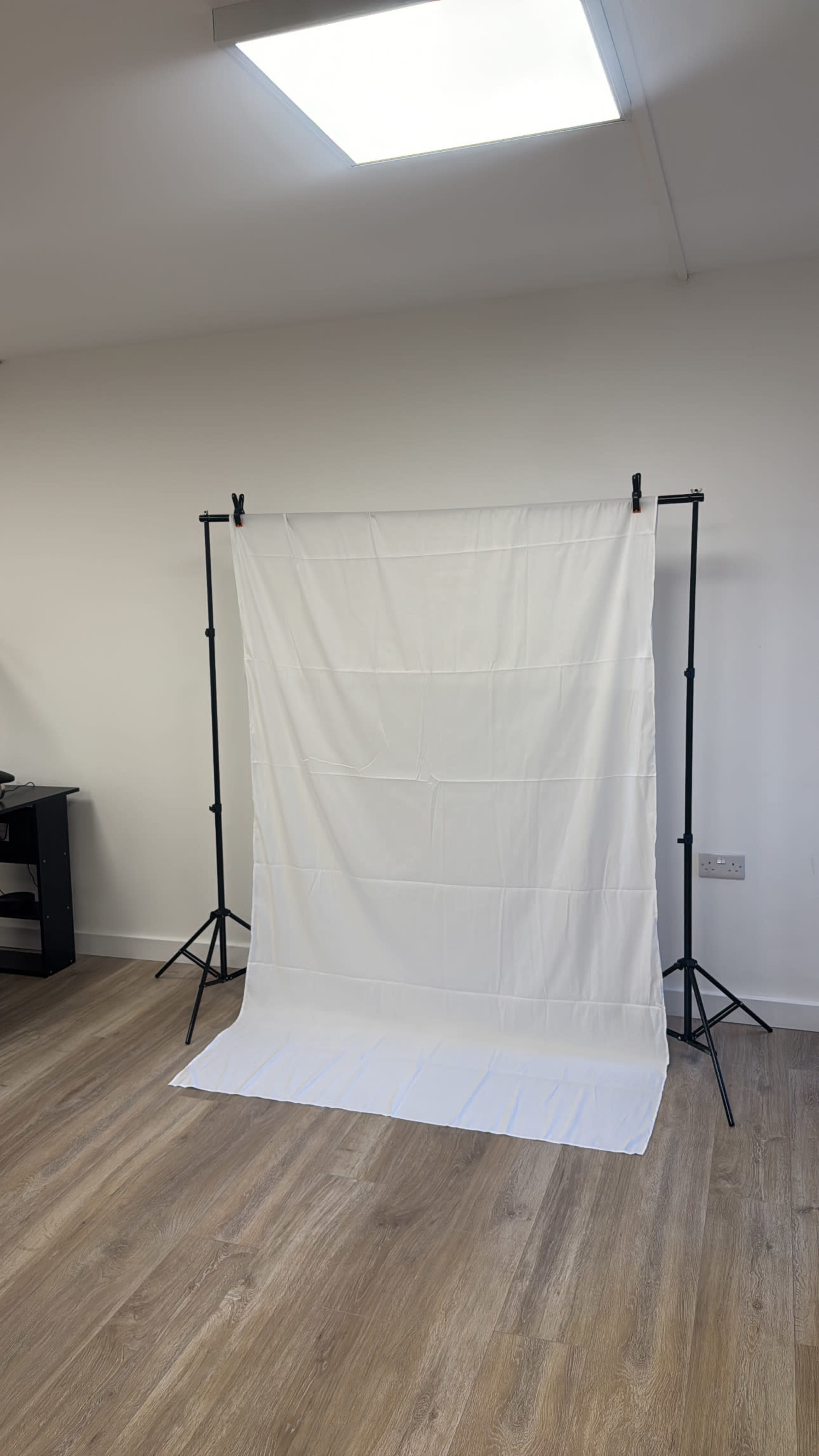 The image shows a white backdrop suspended on a black stand in a well-lit room with wooden flooring.