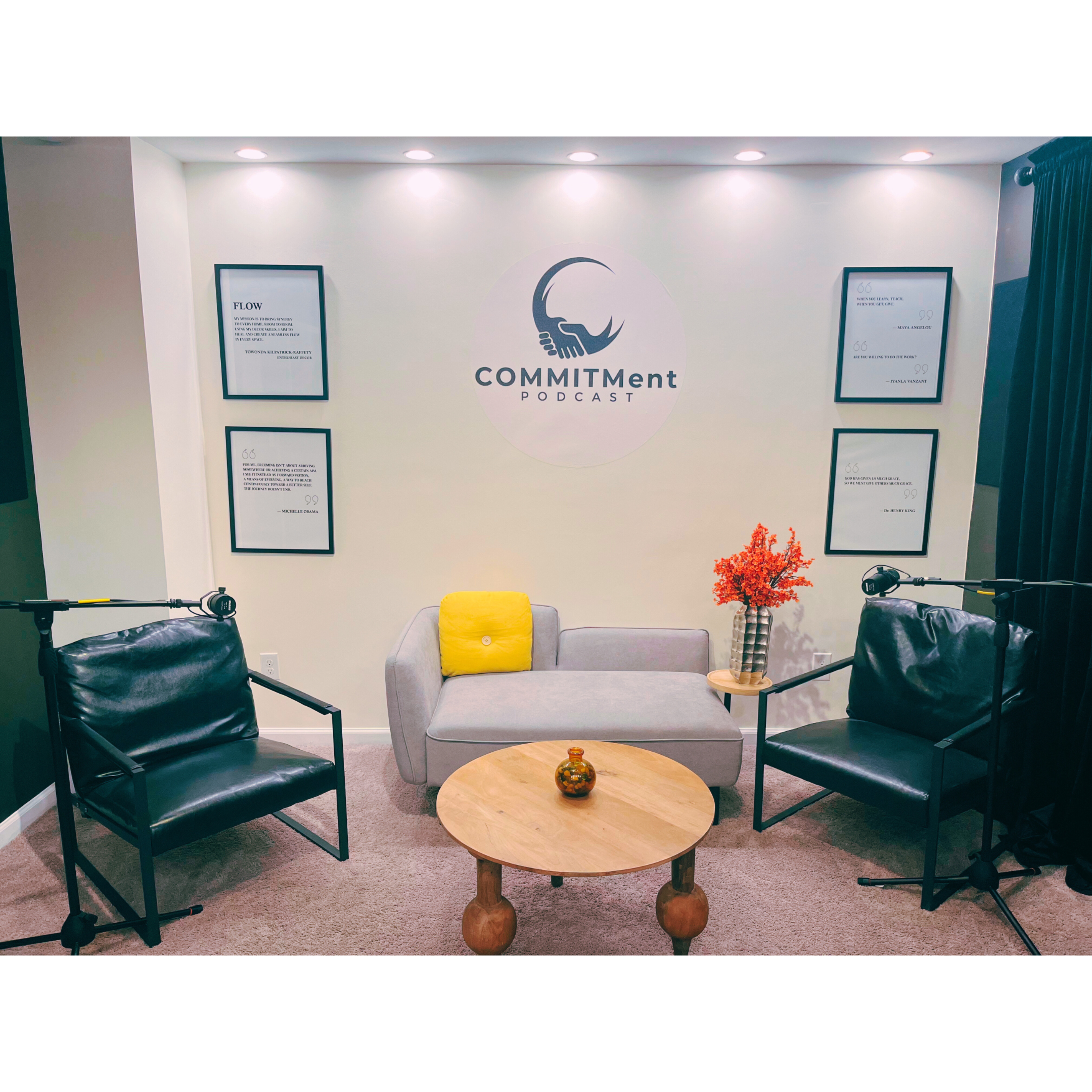 A podcast recording studio featuring two chairs positioned next to a small round table, a sofa, and a decorative plant, with framed quotes on the walls.