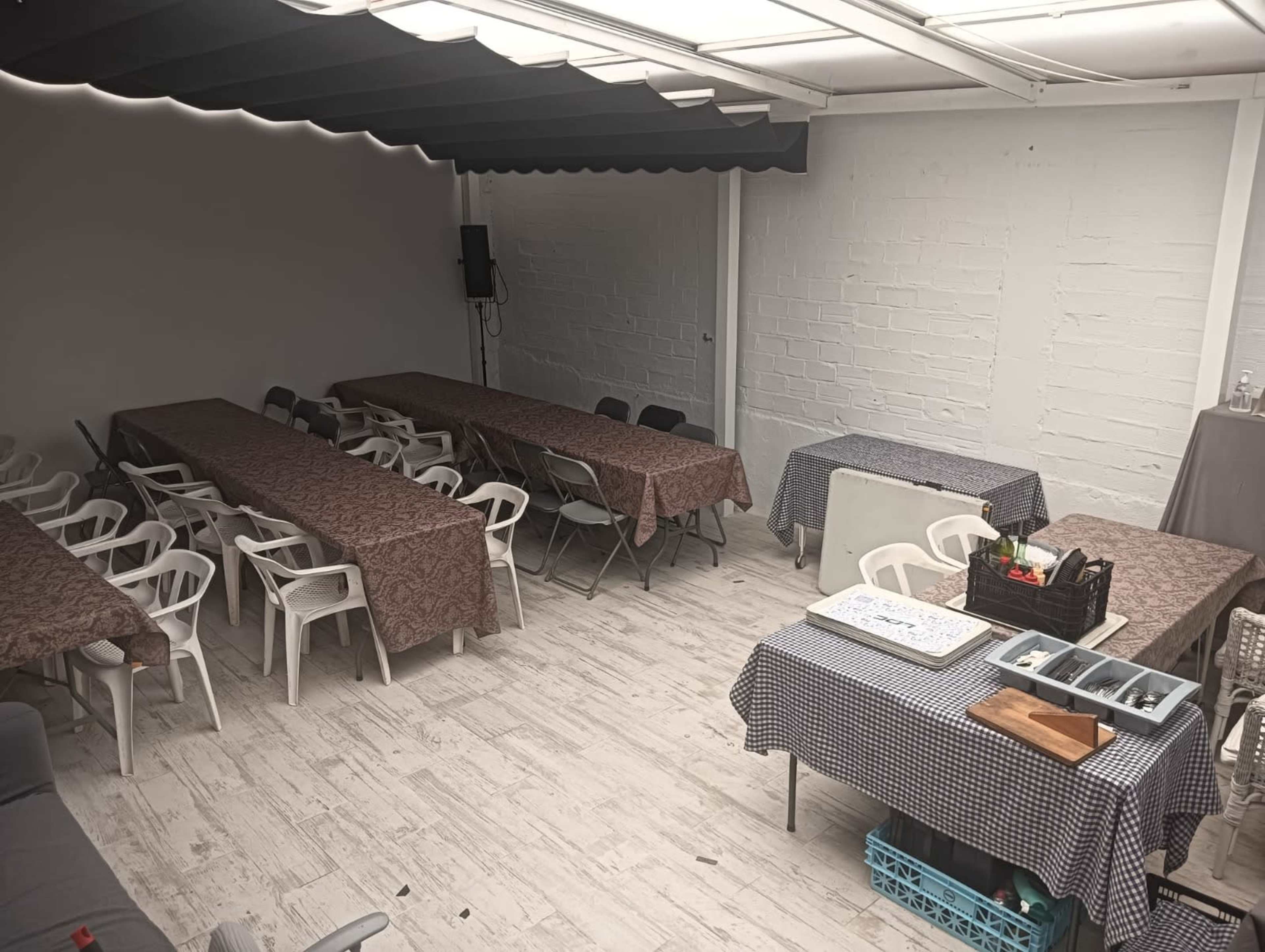 The image shows a workshop or meeting space with multiple tables covered in cloth and arranged with plastic chairs around them.