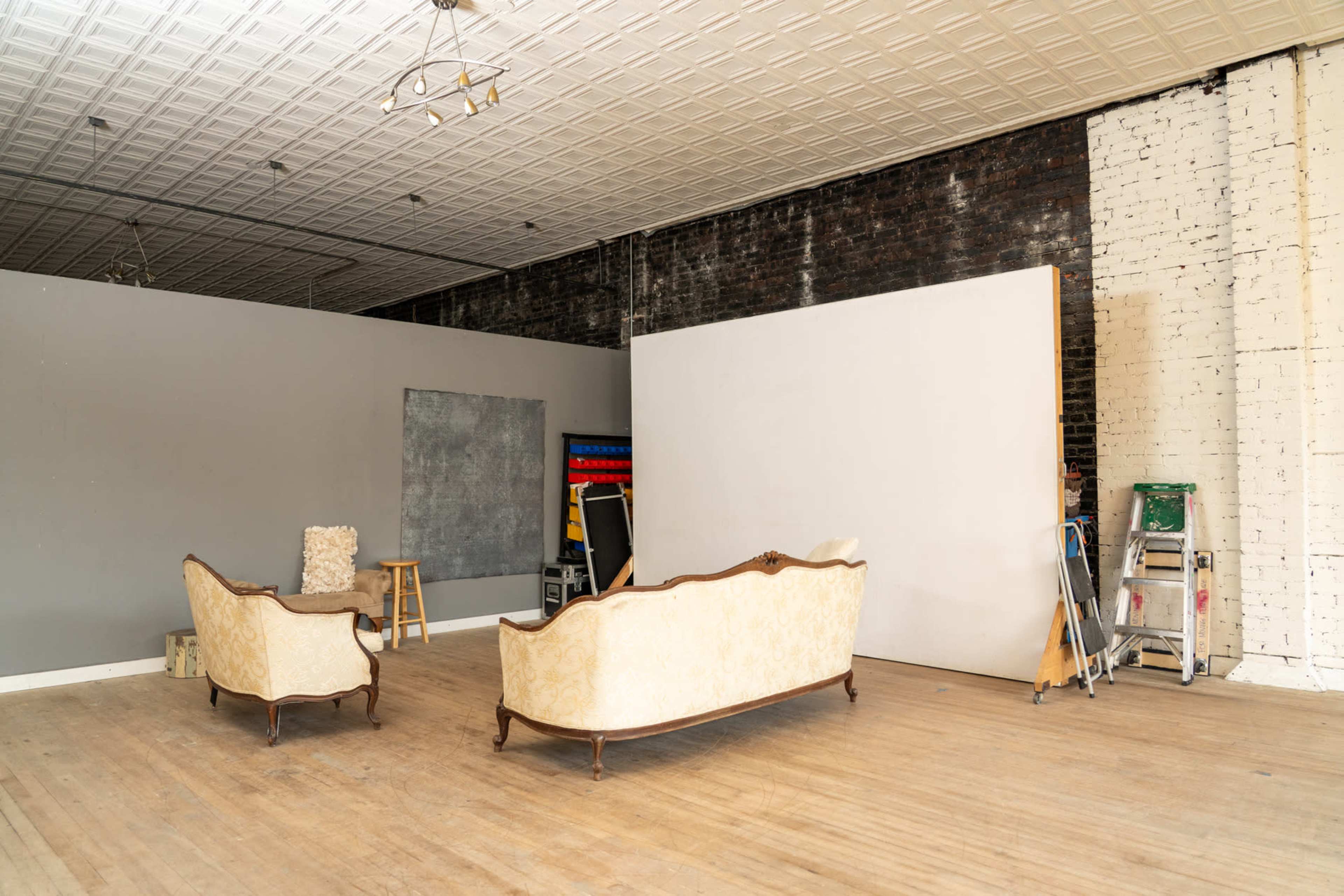 The image shows a spacious interior featuring two vintage sofas facing a blank wall, with a stool and art supplies nearby.