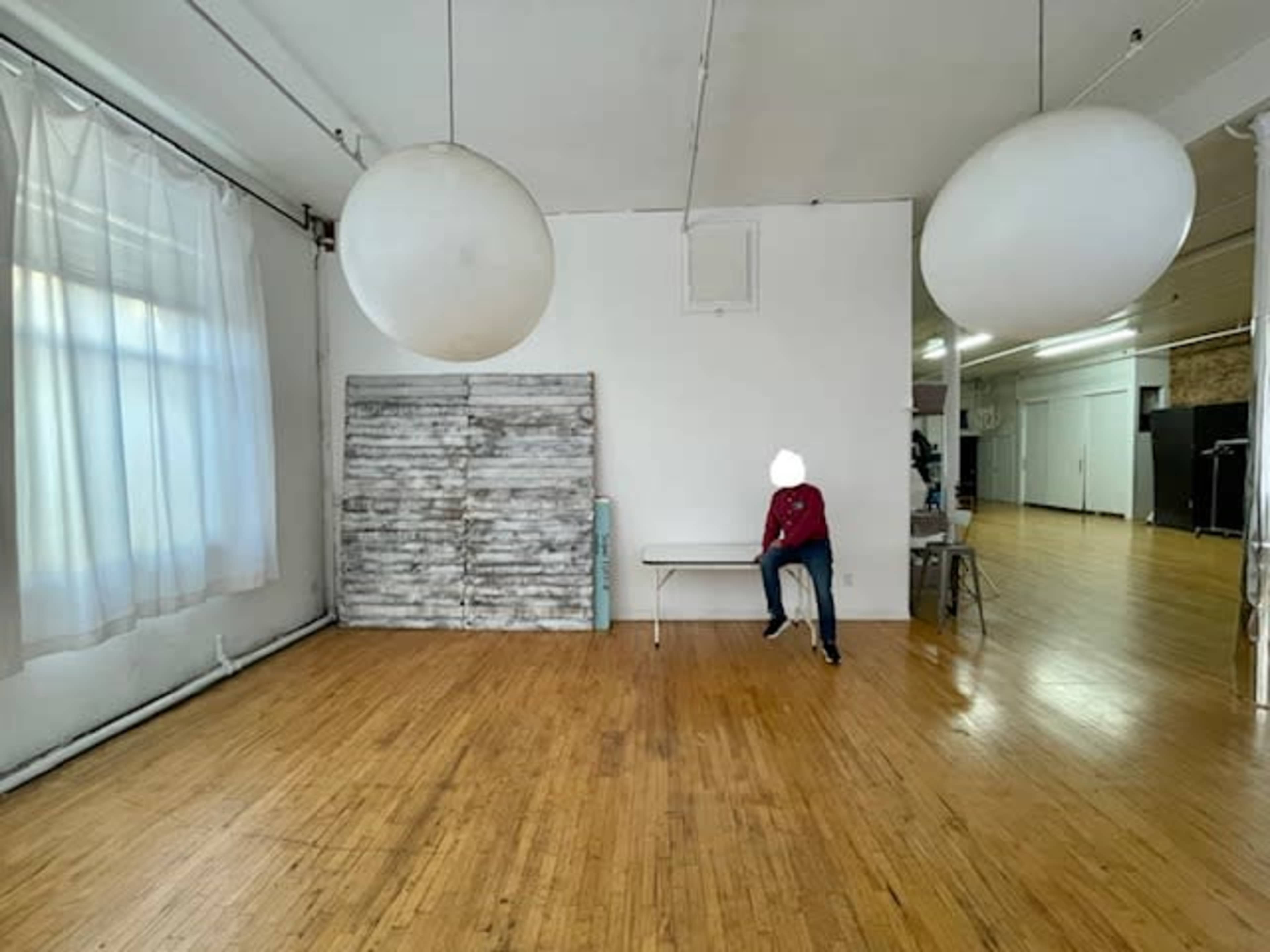 A spacious room features large hanging light fixtures, a wooden floor, a bench, and a wall with a rustic wooden panel.