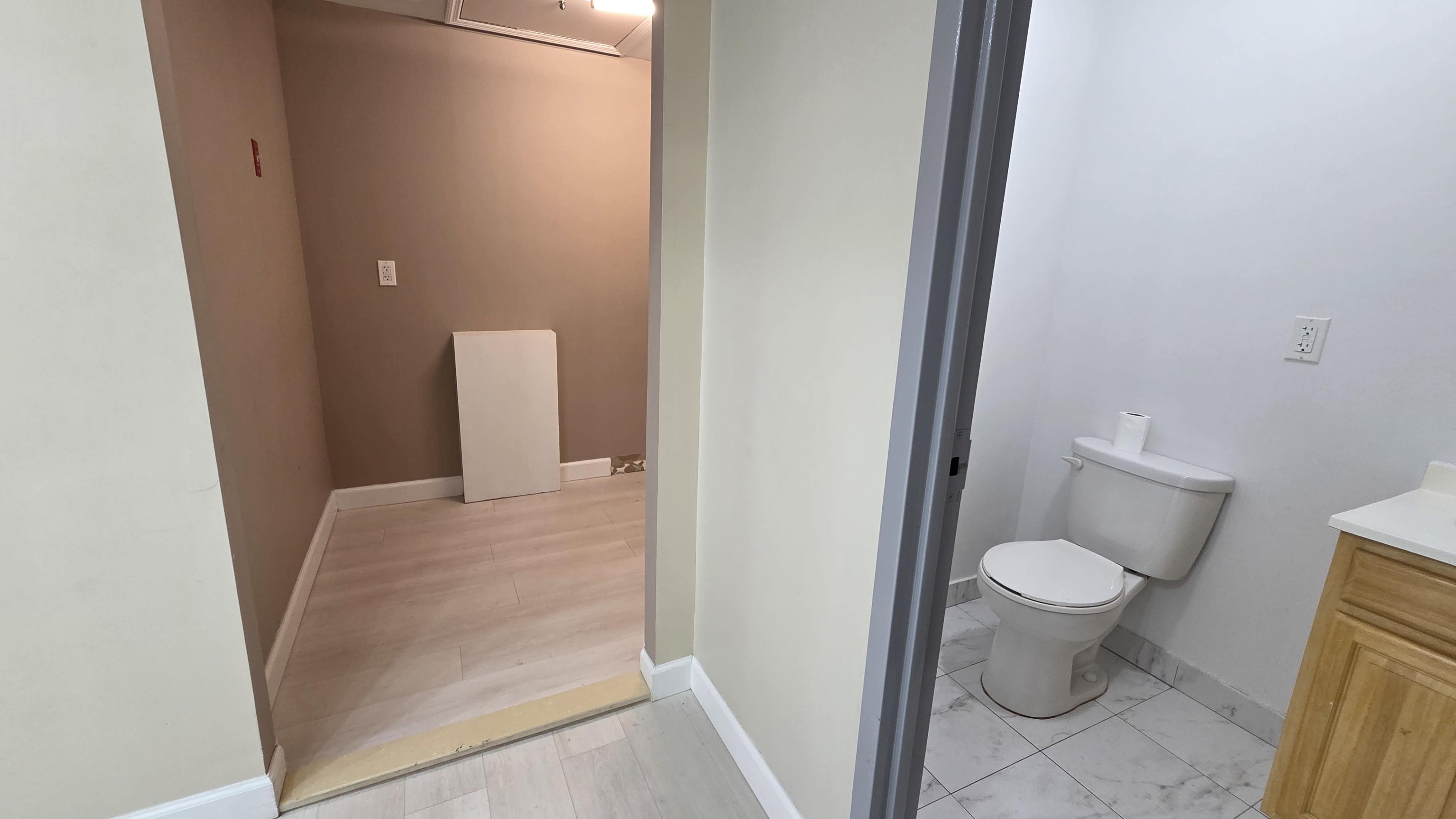 The image shows a small hallway leading to a bathroom on the right, with an empty room visible ahead.