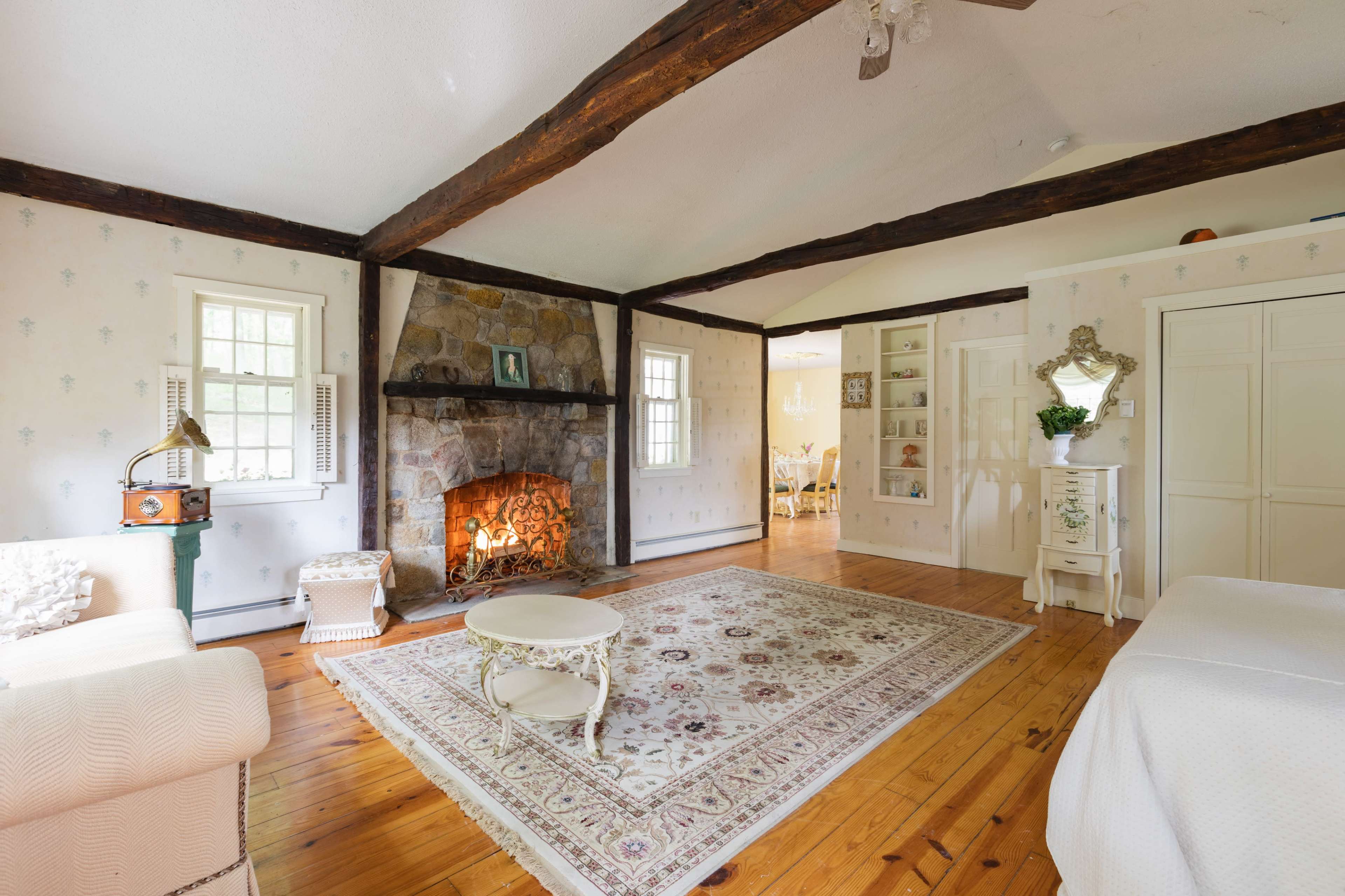 The image shows a spacious living room with a stone fireplace, hardwood flooring, and large windows allowing natural light to enter.