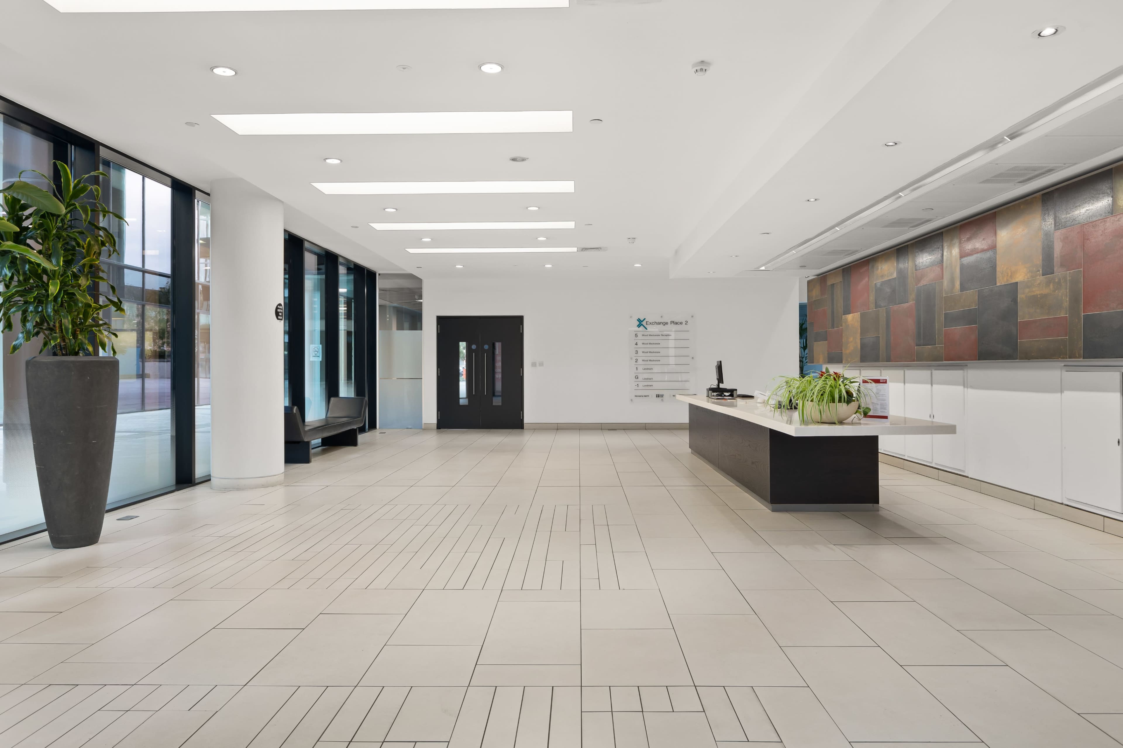 A modern office lobby with a reception desk, large glass windows, and potted plants.