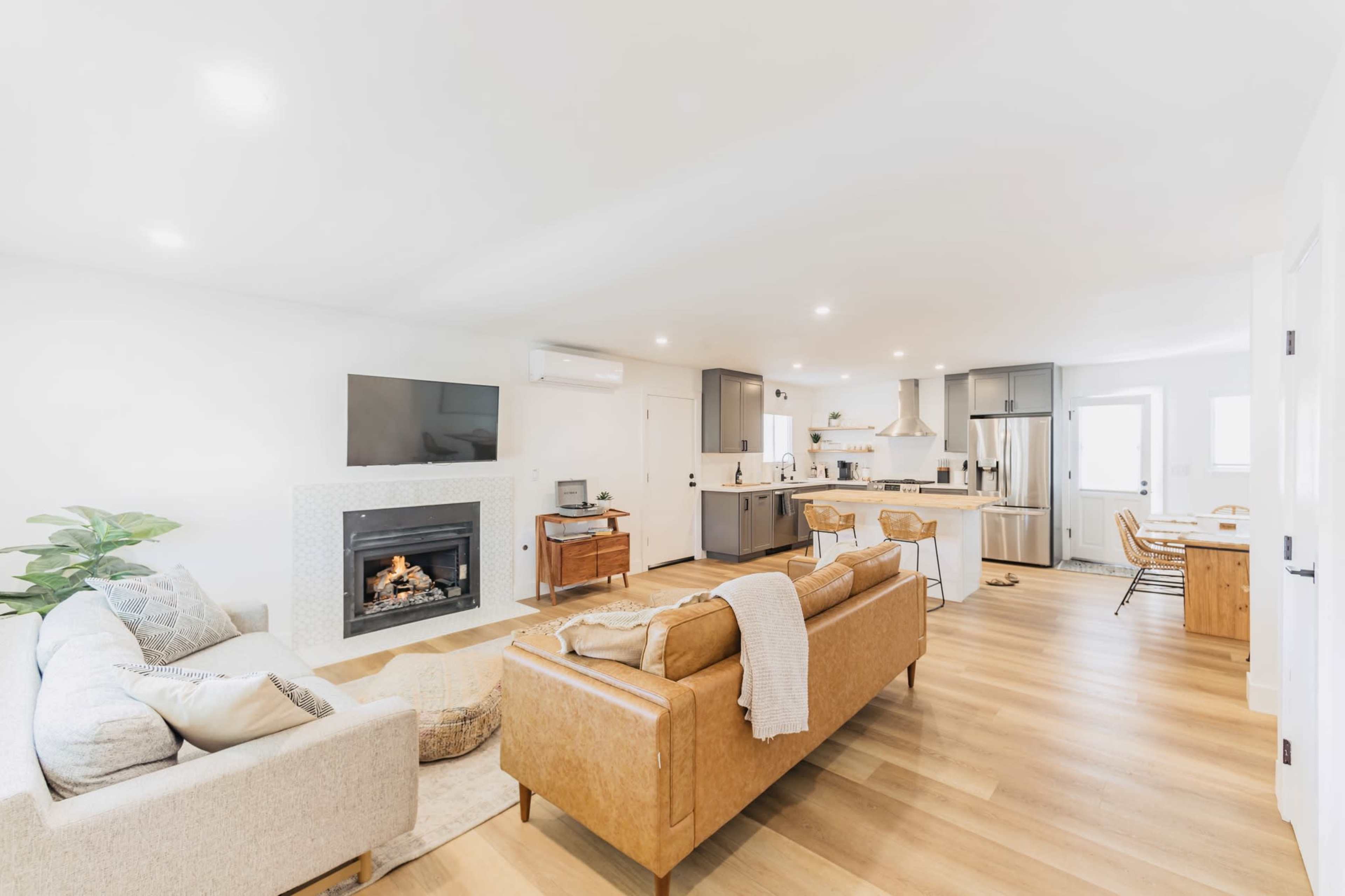 The living area features a fireplace with a television above it, two couches, a dining table, and a kitchen in an open layout.