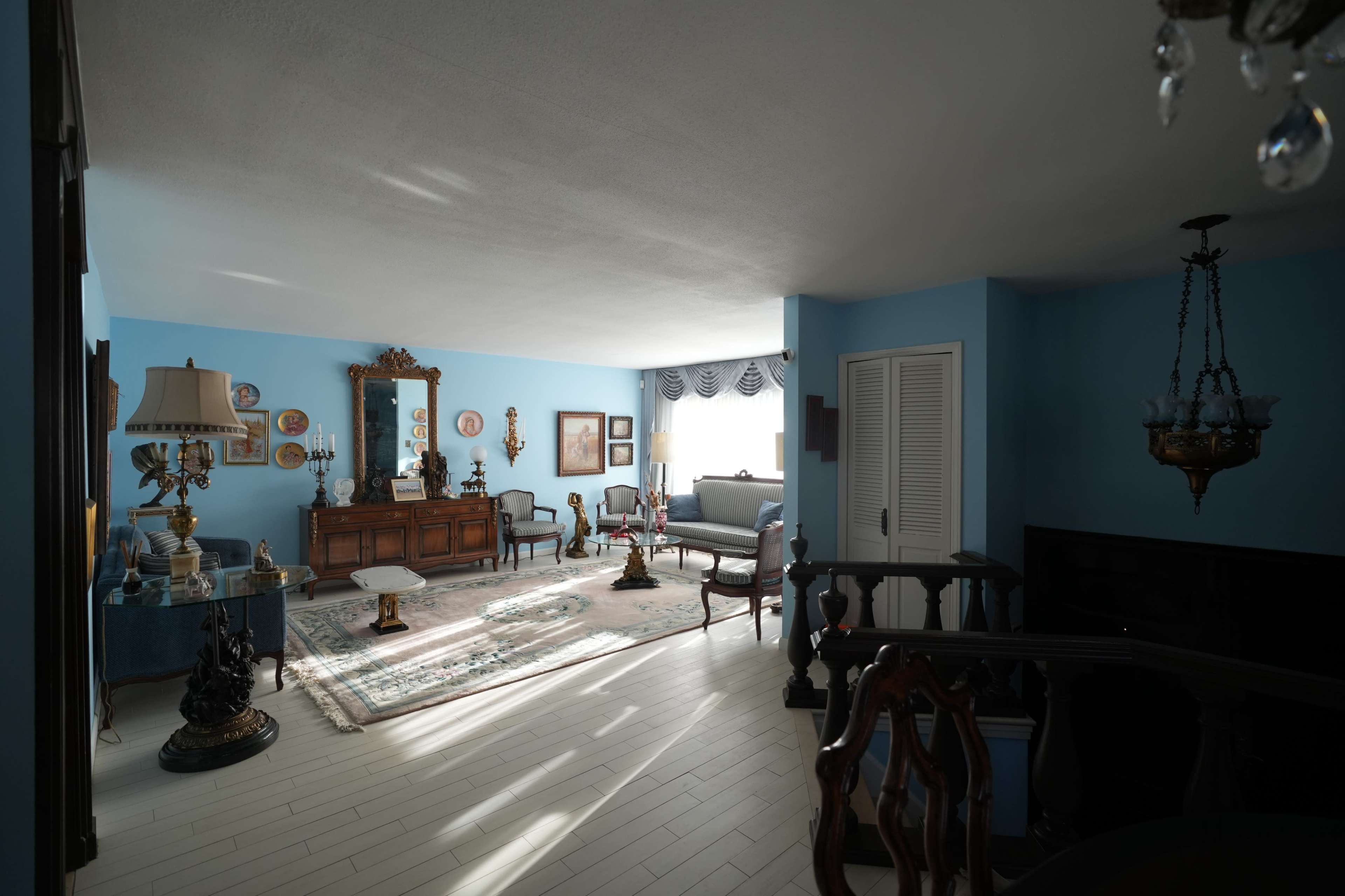 The image depicts a well-furnished living room with blue walls, vintage furniture, and decorative elements including a large mirror and a chandelier.