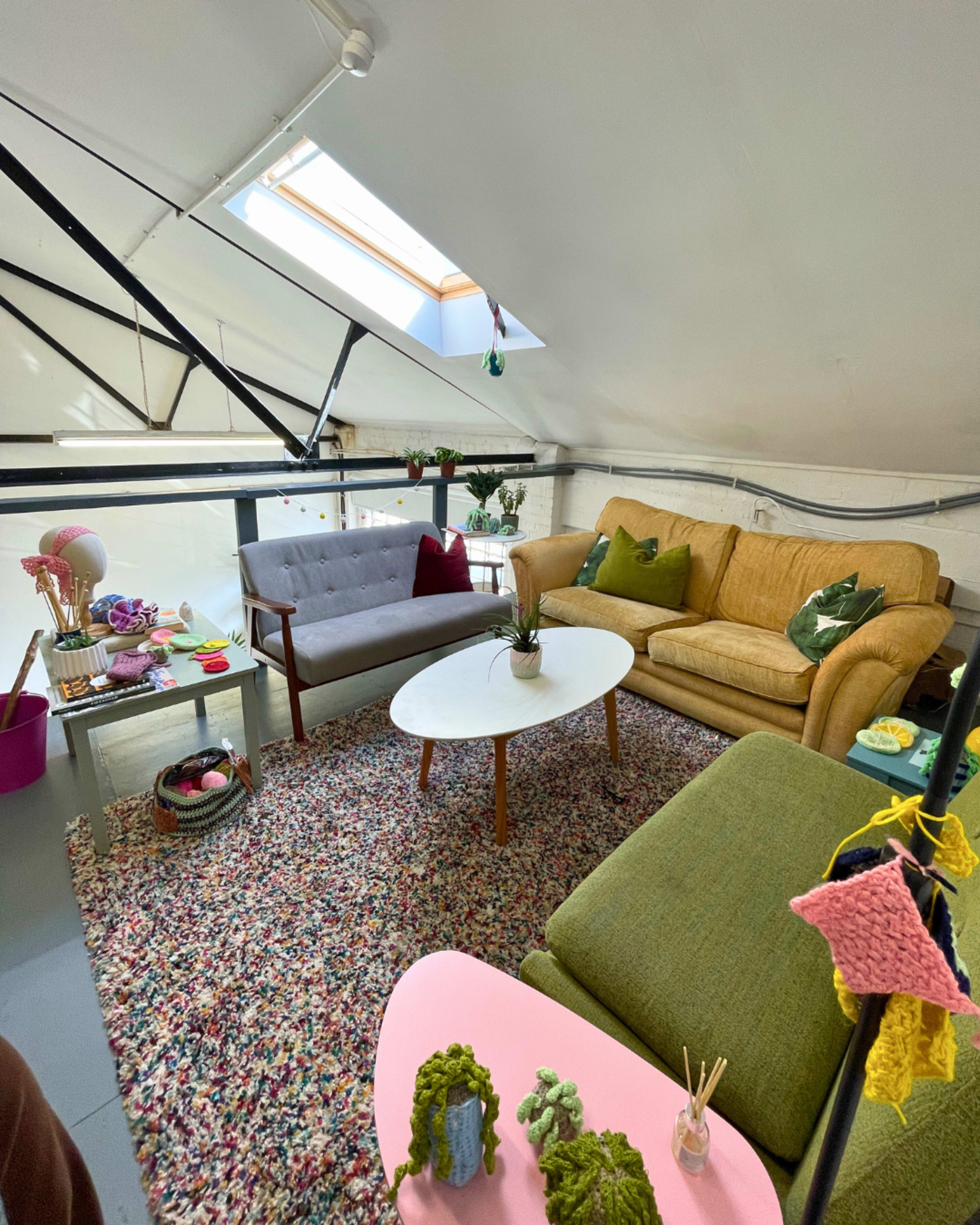 The image shows a cozy attic living space furnished with sofas, a coffee table, and decorative plants, all arranged on a colorful rug.