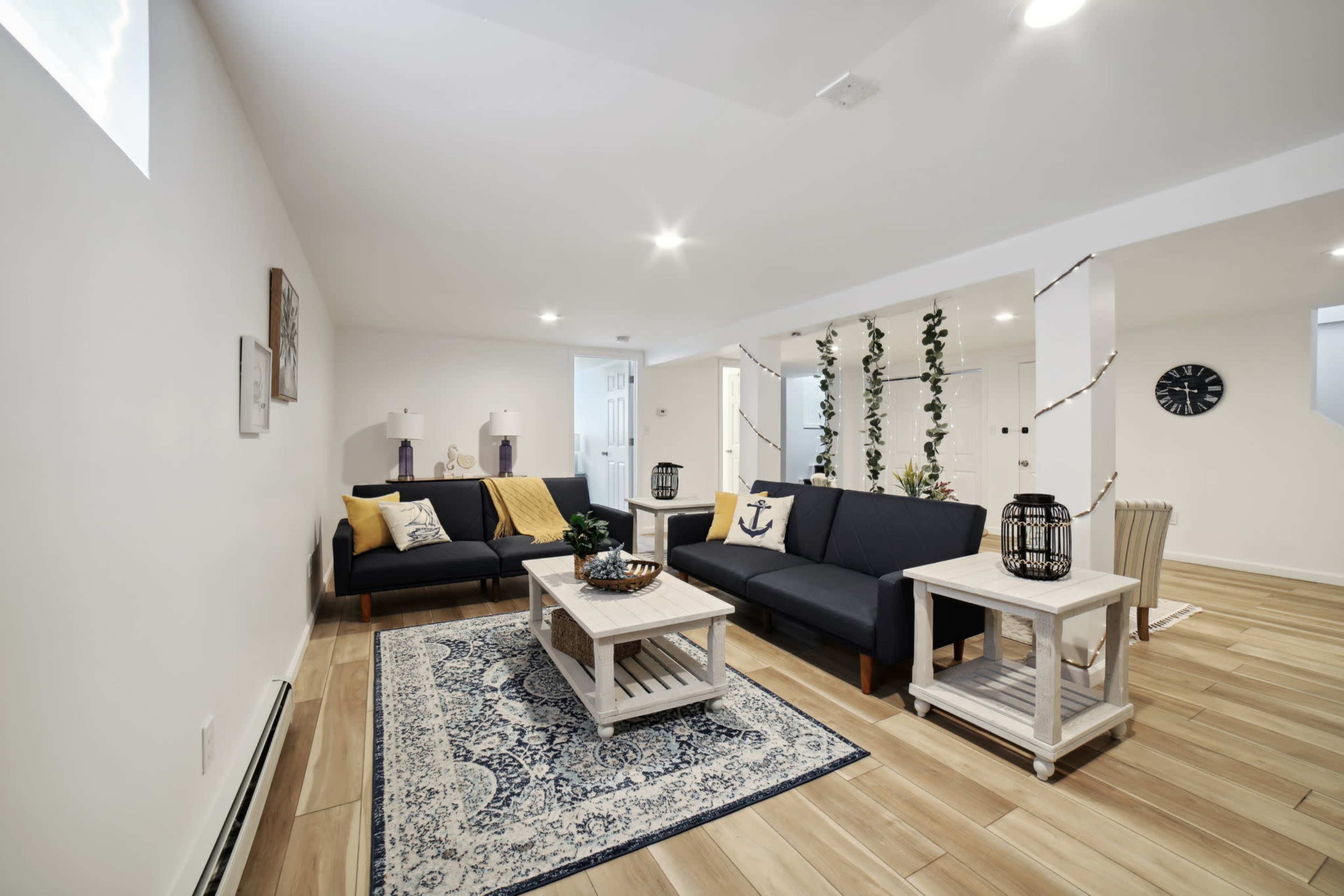 A modern living room with black sofas, a wooden coffee table, and decorative plants against a light-colored wall.