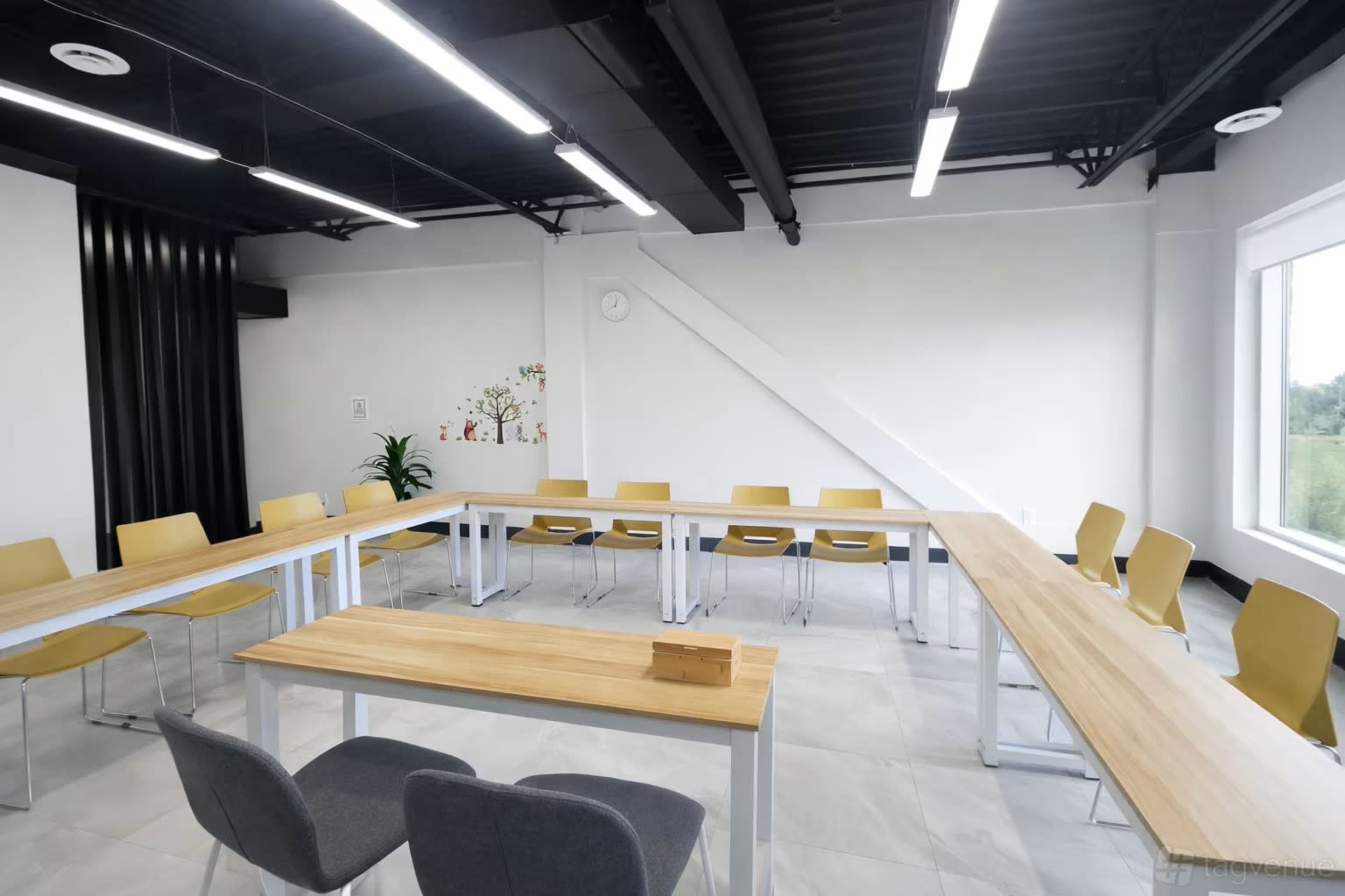 The image shows a modern meeting room with a large, rectangular table surrounded by yellow and gray chairs, and a bright window providing natural light.