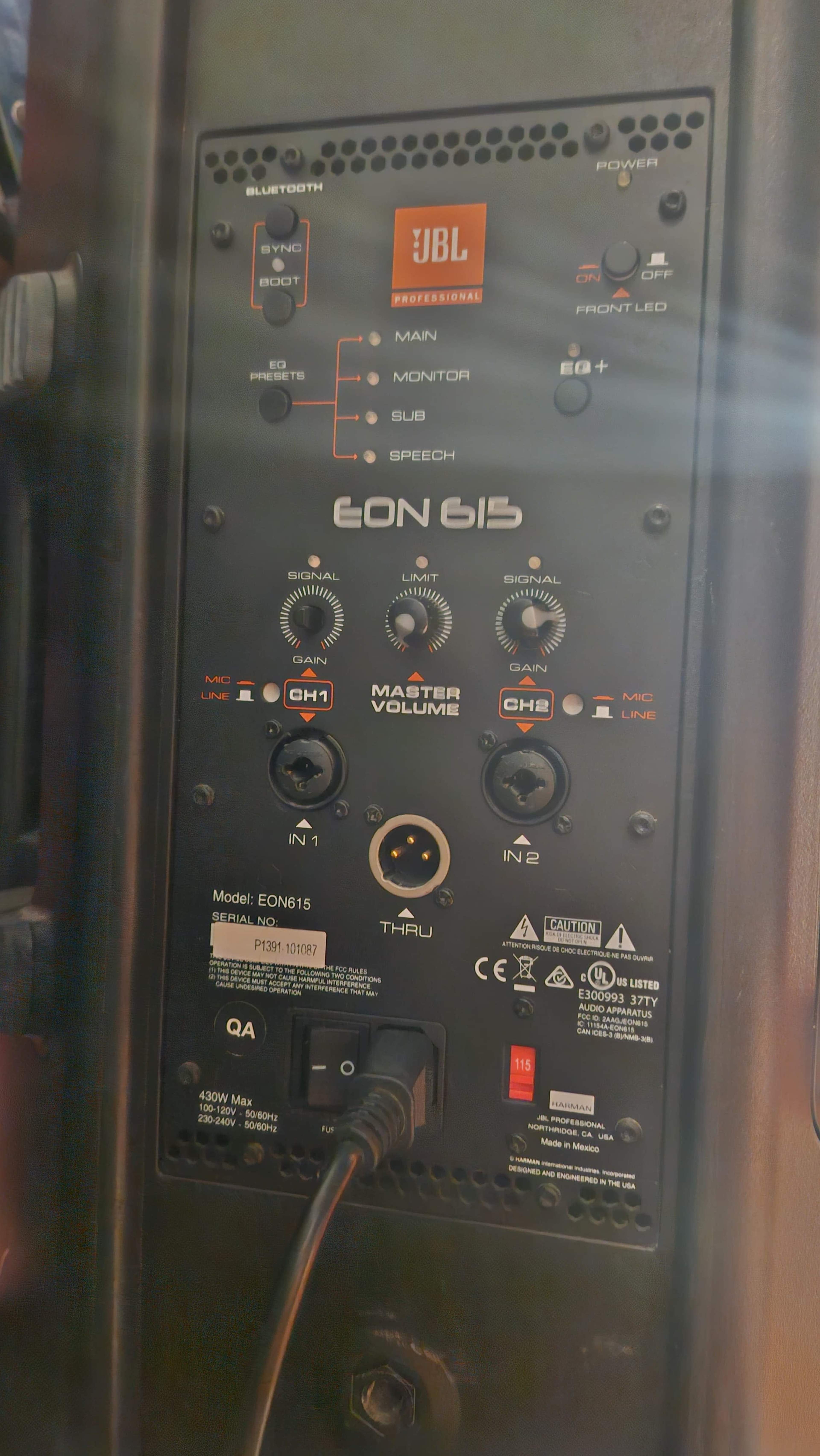 The image shows the control panel of a JBL EON615 speaker, featuring various knobs for input and volume adjustments, along with Bluetooth and power indicators.