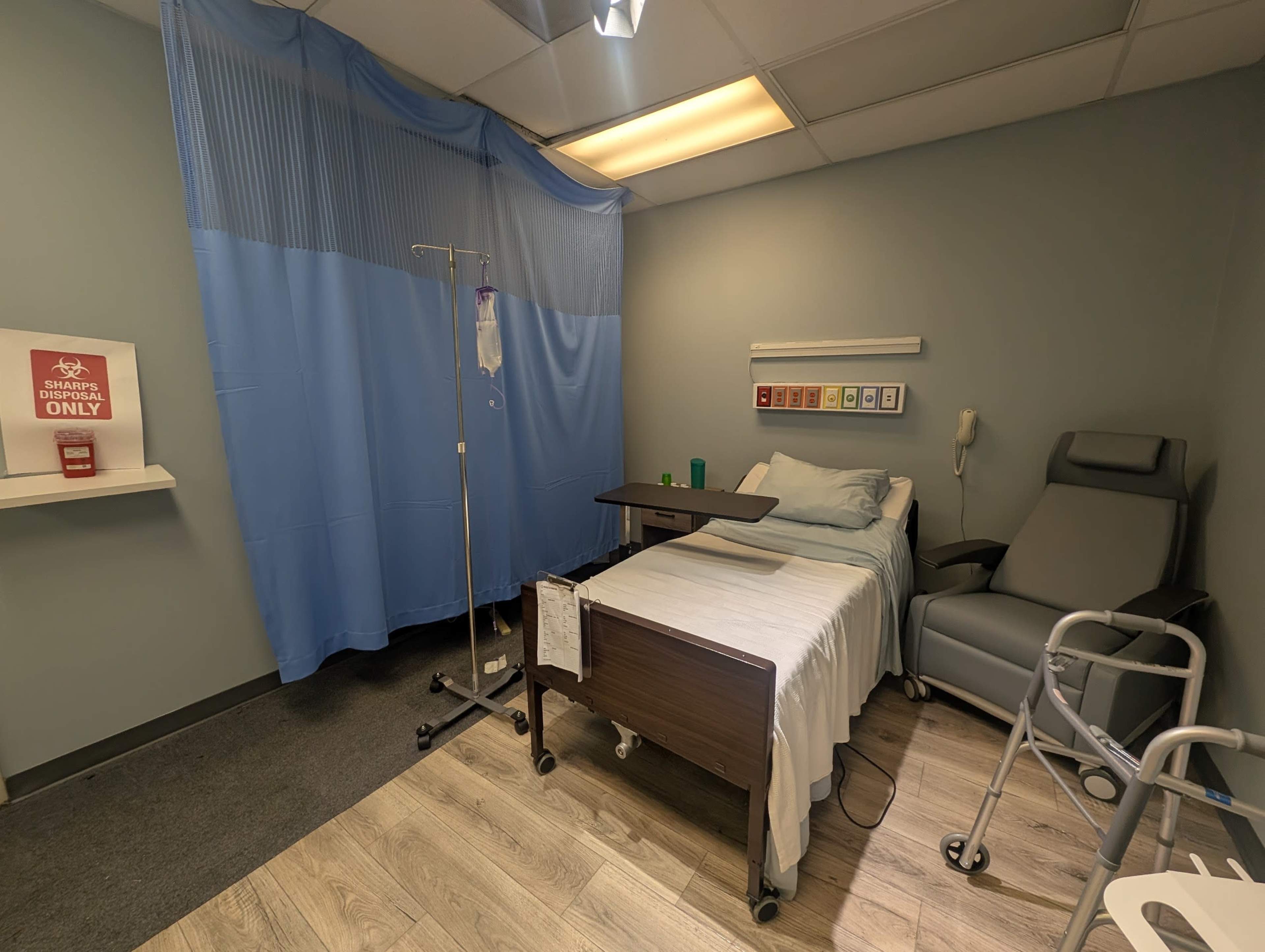The image shows a hospital room with a bed, an IV stand, a recliner chair, and a privacy curtain.