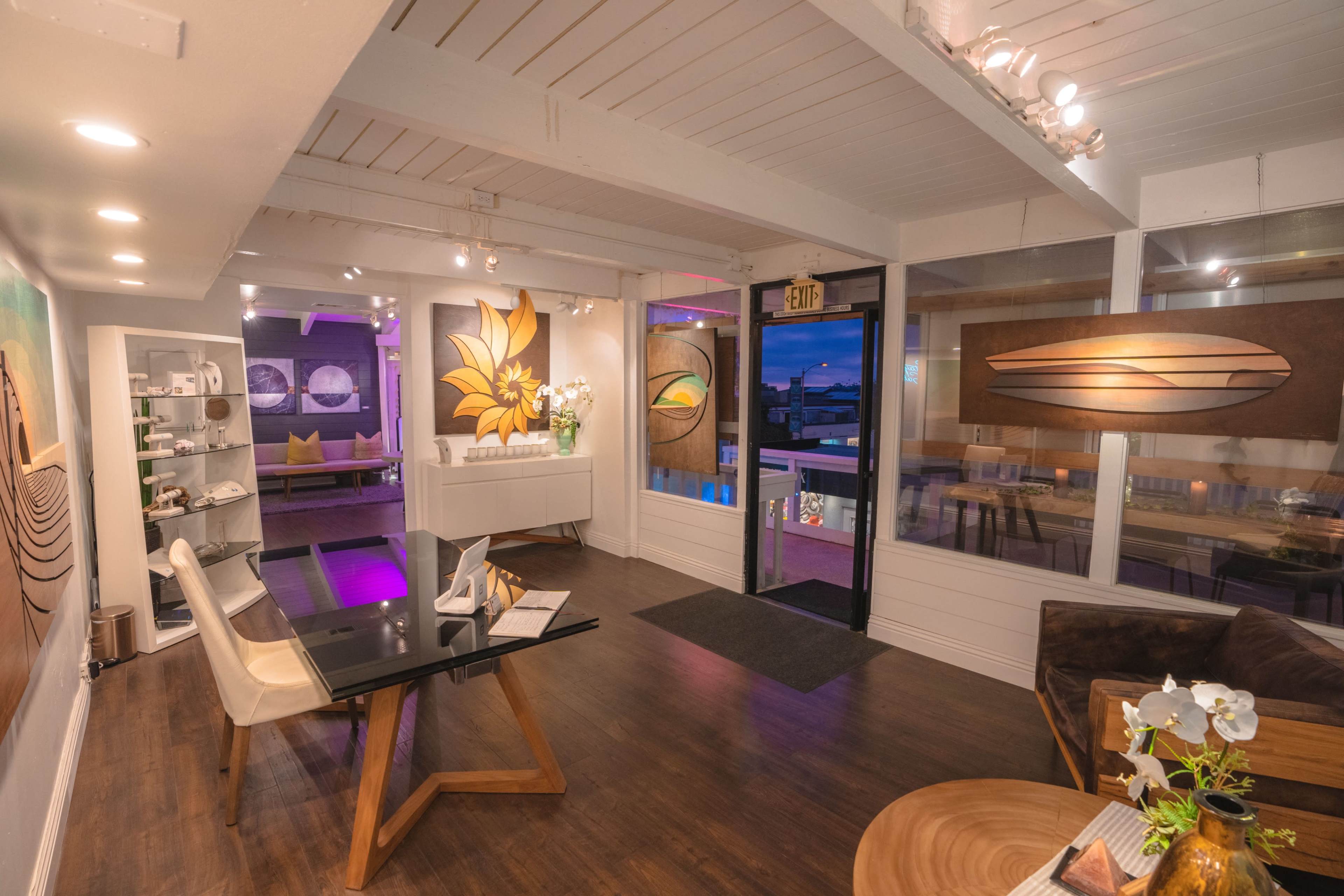 A modern interior space with wooden floors, a table and chairs, decorative wall art, and large windows featuring a view outside.