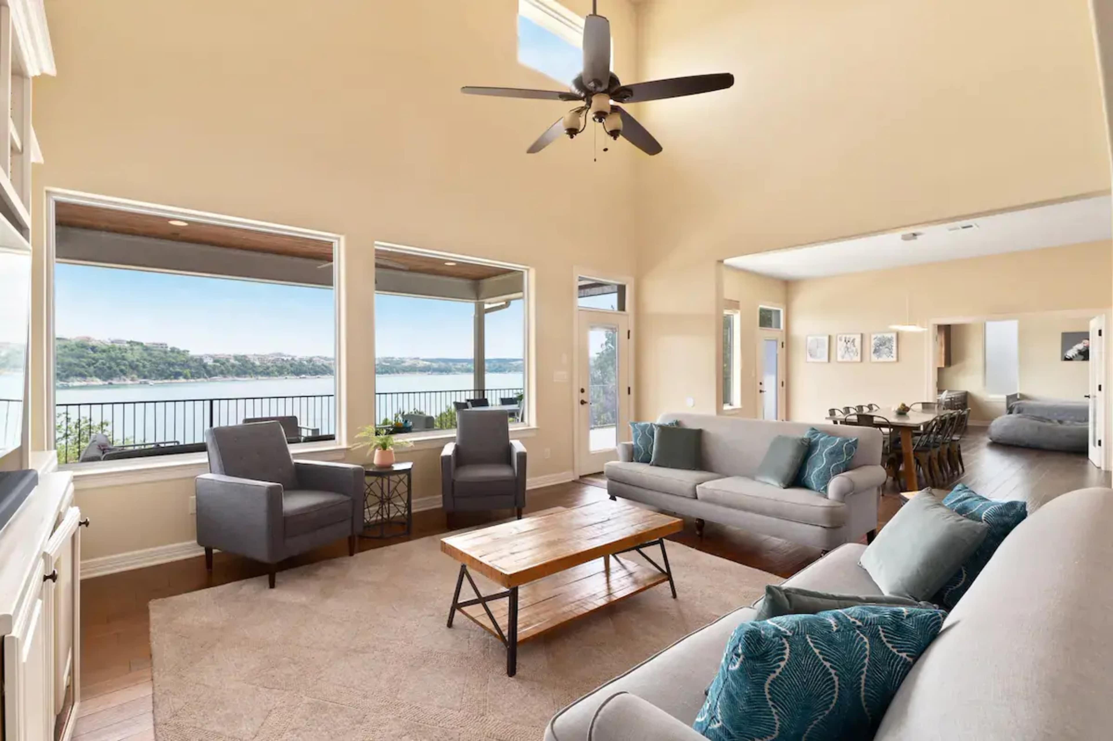 A spacious living room with large windows overlooking a body of water and furnished with a coffee table, two armchairs, and two sofas.