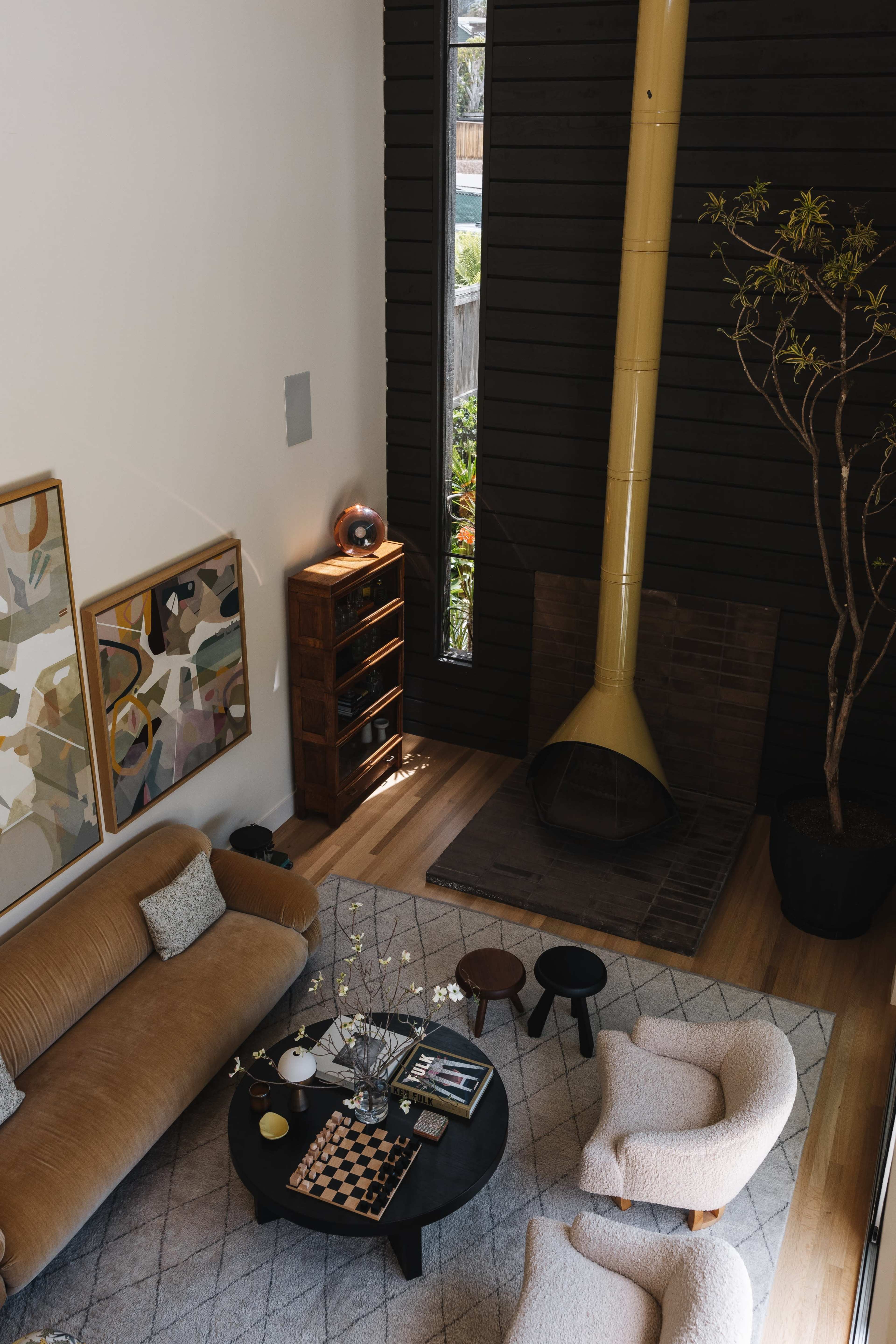 The image shows a modern living room with a beige sofa, two white armchairs, a black coffee table, and a tall yellow chimney in a corner.
