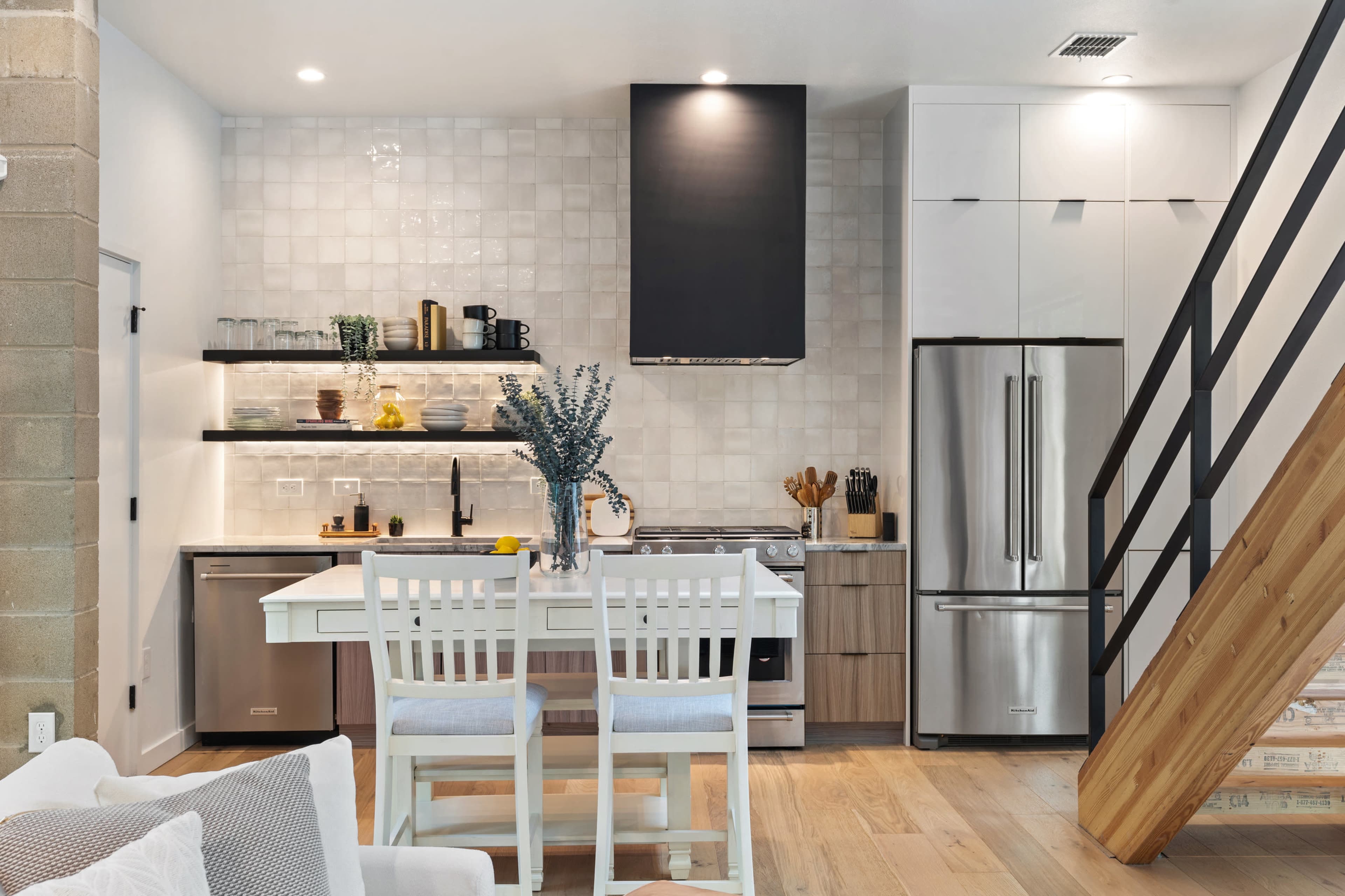A modern kitchen features stainless steel appliances, wooden cabinetry, and a dining table with white chairs.