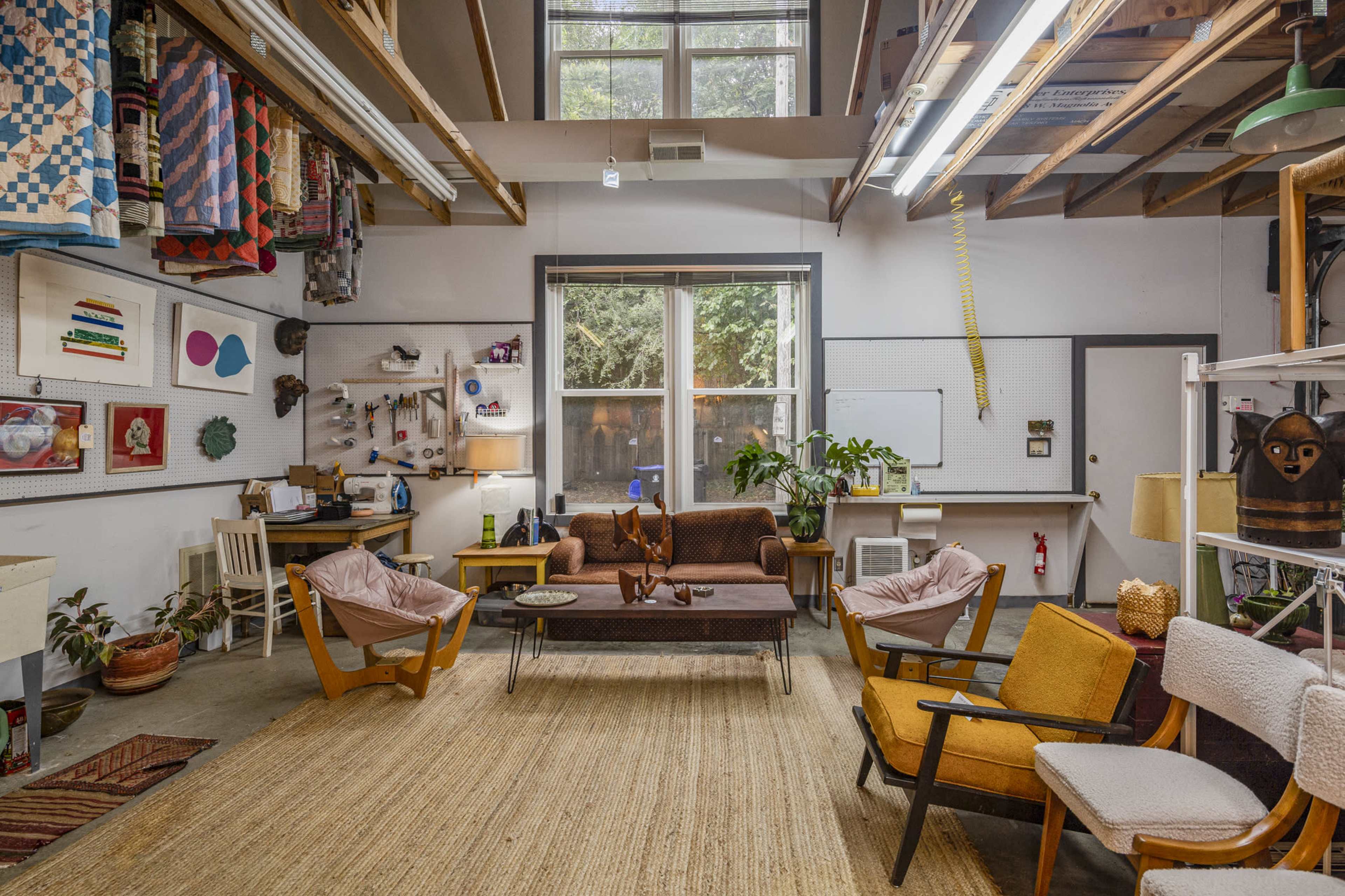 A creatively arranged workshop or studio space with a central seating area, large windows, and decorative items on the walls.