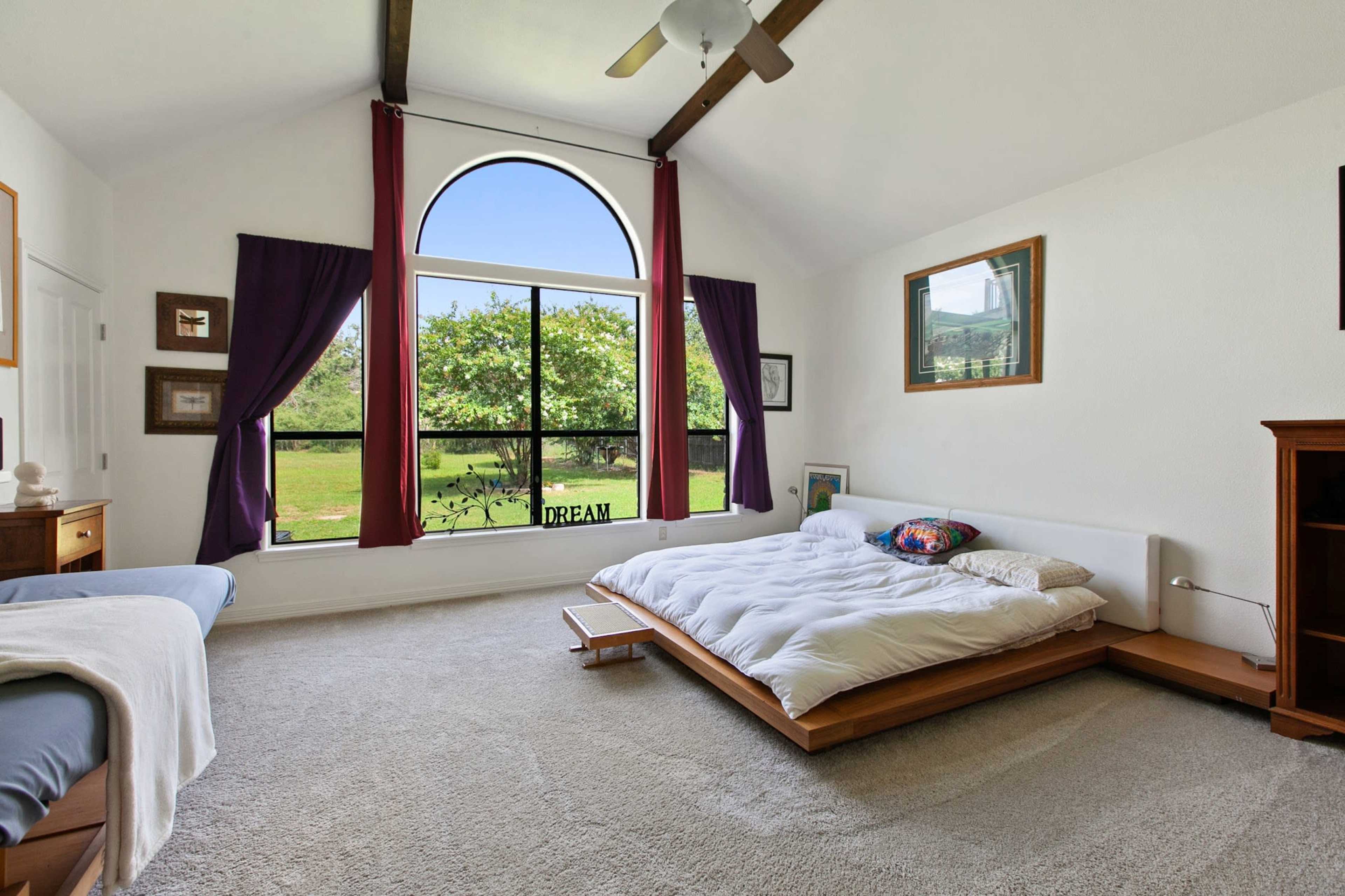 A spacious bedroom with a large window overlooking greenery, featuring a low wooden bed and a seating area.