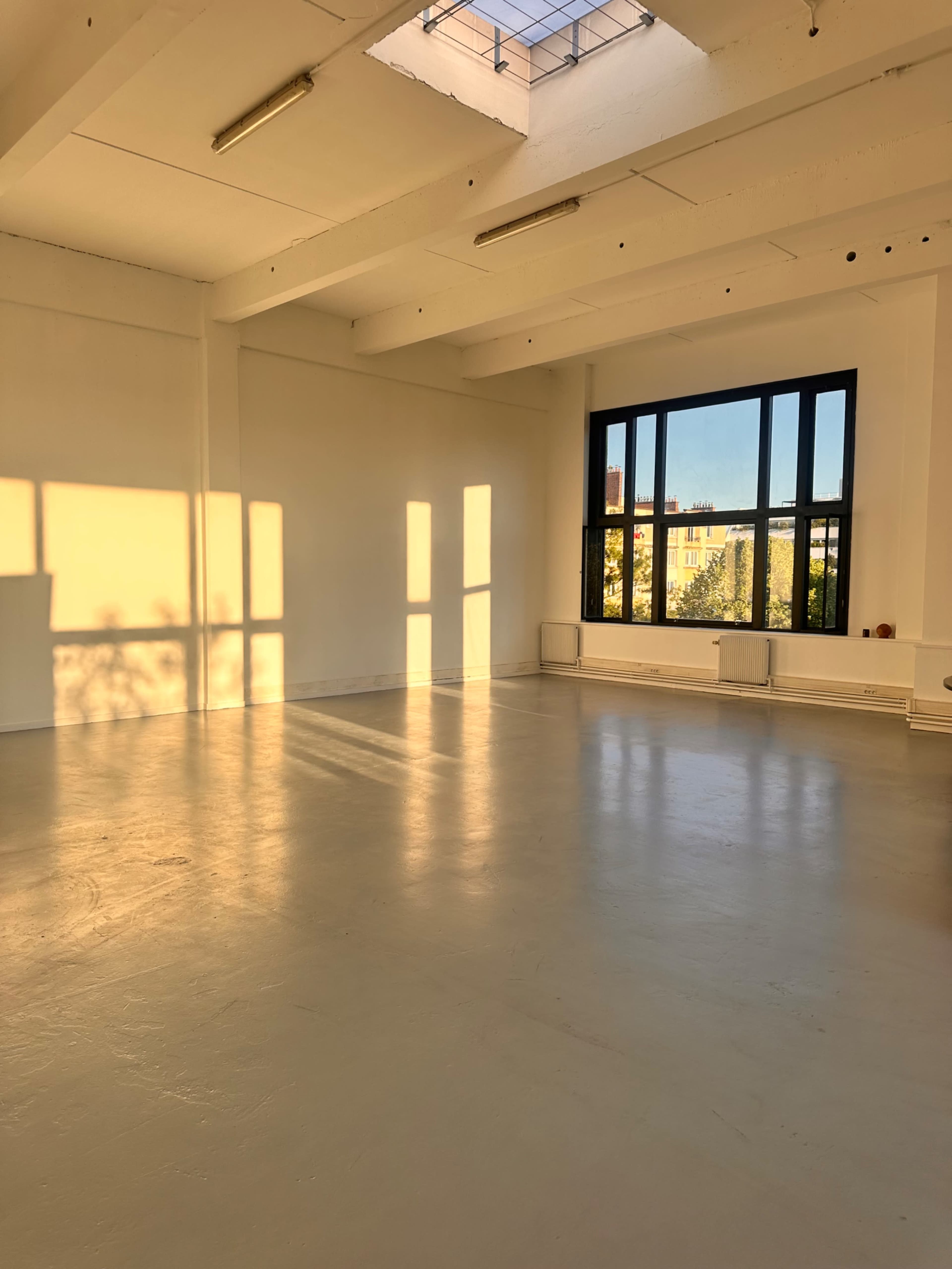 A bright, empty room with large windows, allowing sunlight to cast shadows on the floor.