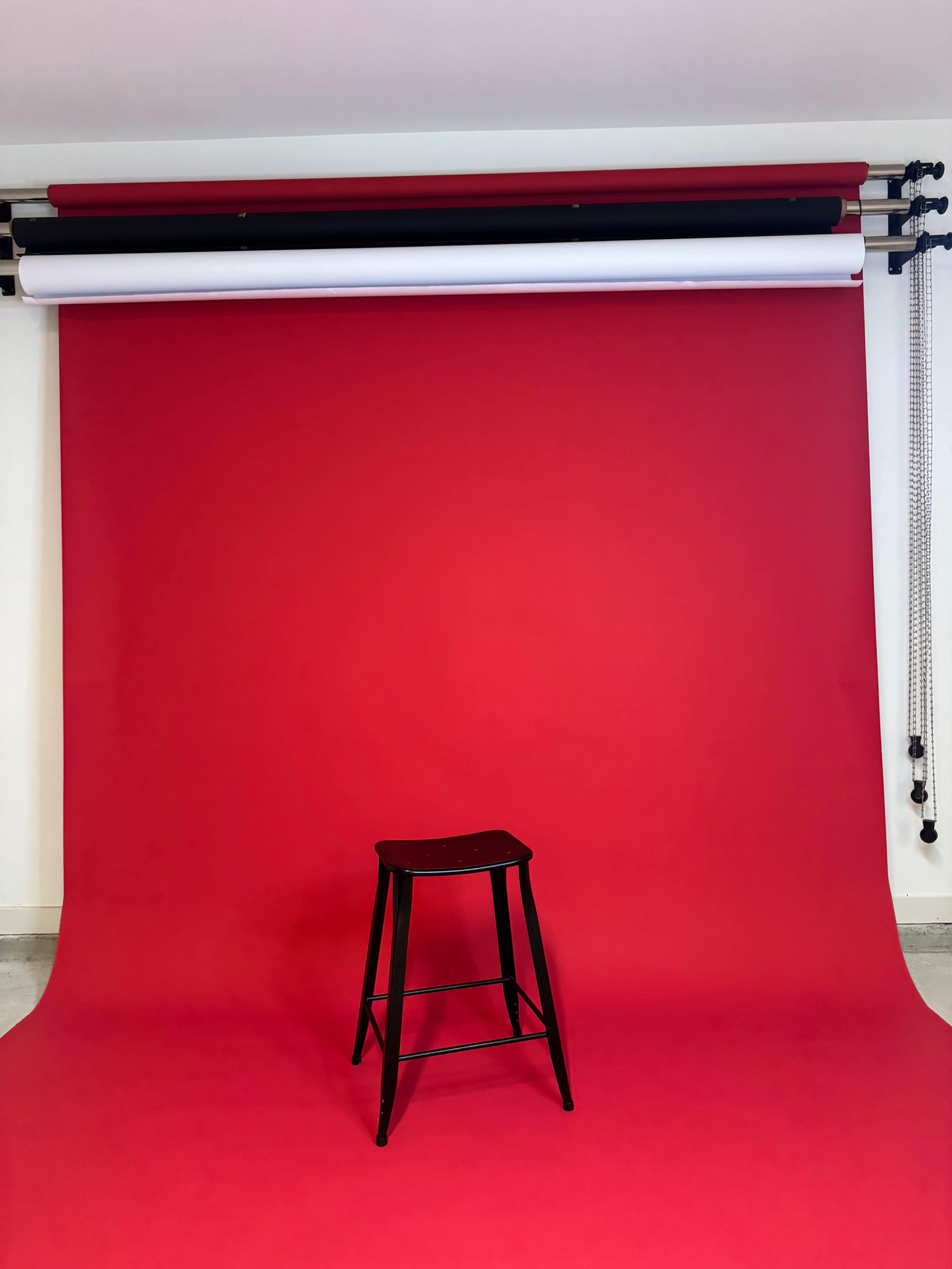 A black stool is positioned in front of a bright red backdrop in a studio setting.
