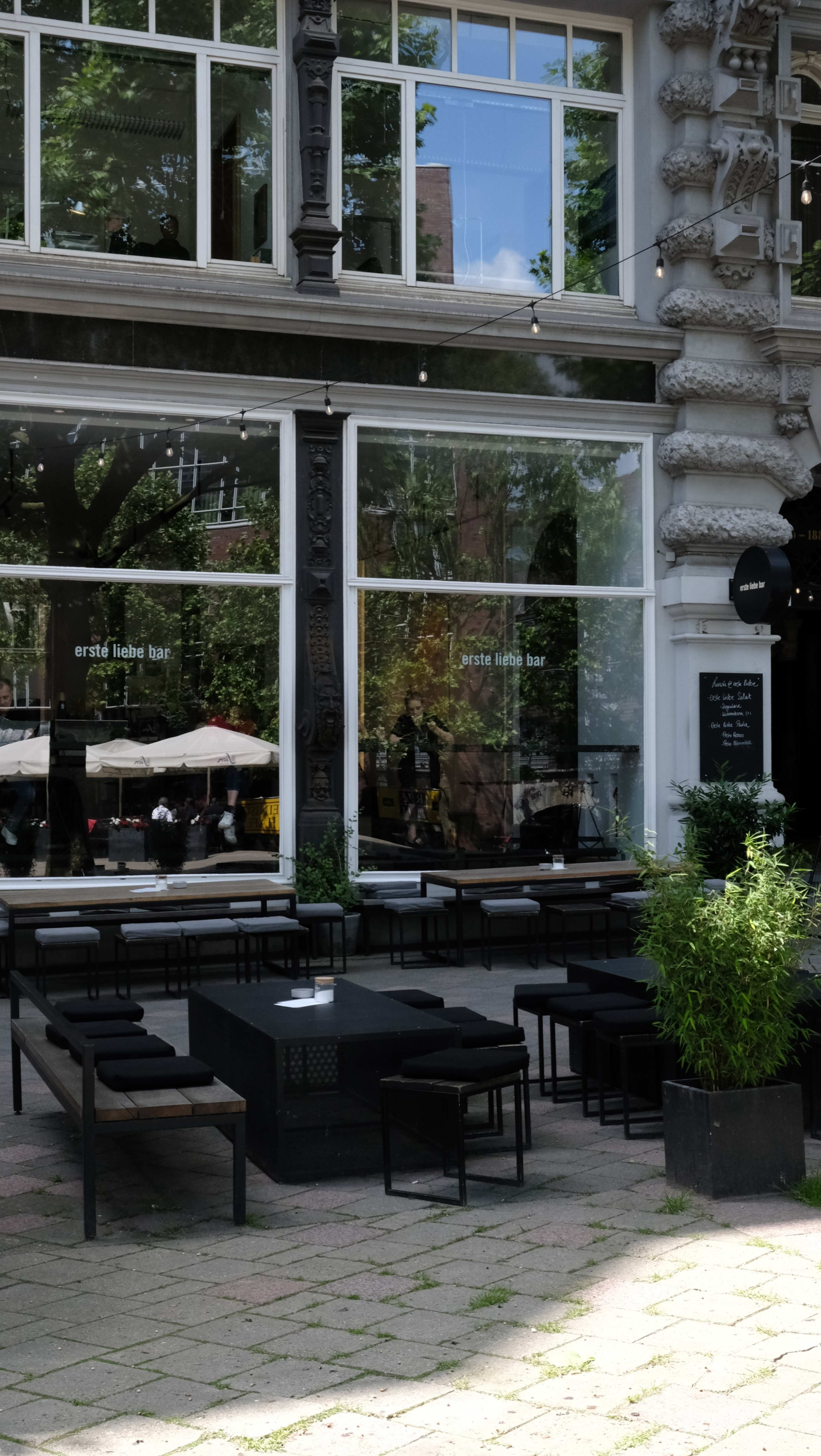 A modern outdoor seating area features black benches and tables in front of a building with large windows and greenery.