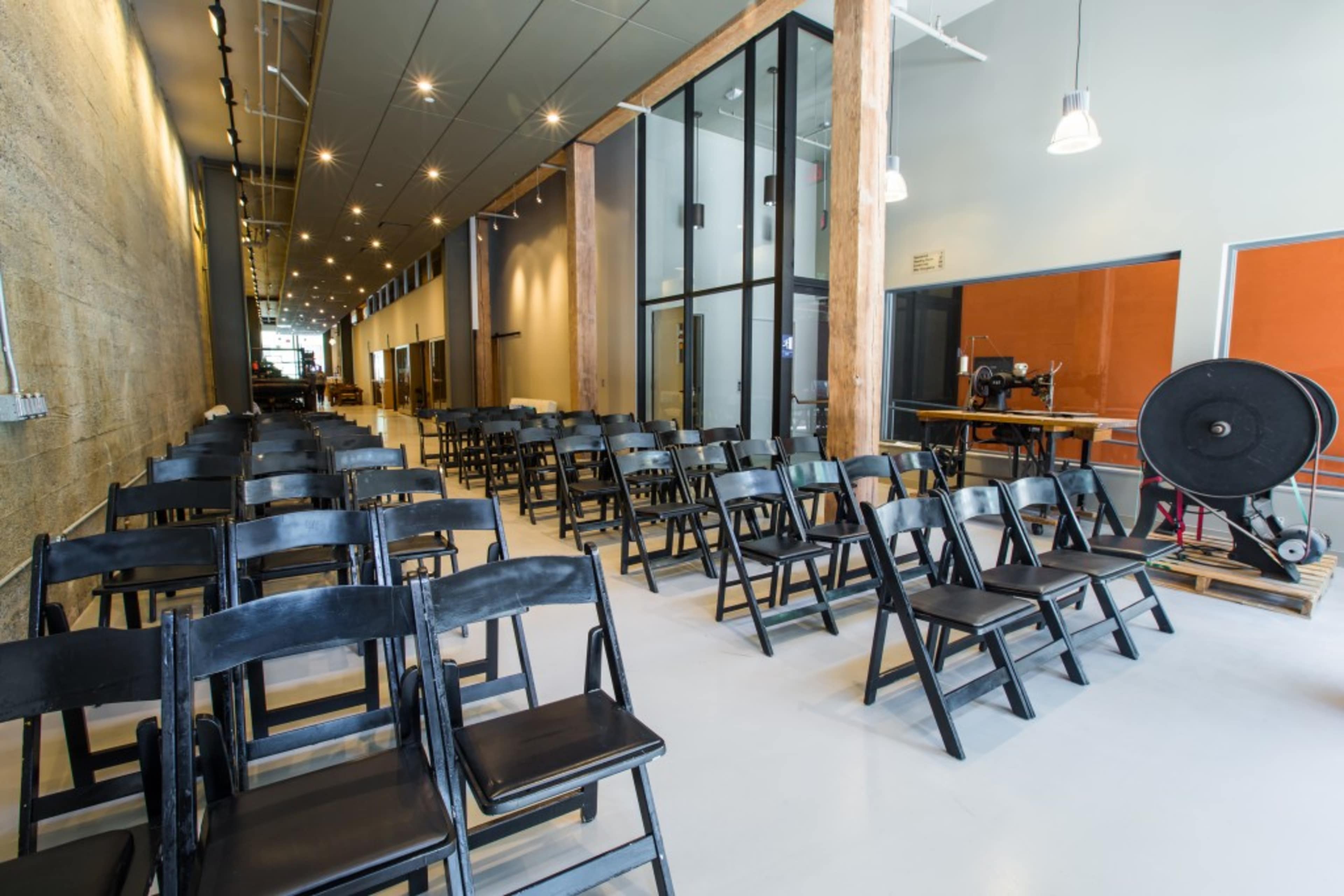 The image shows a spacious room with rows of black folding chairs arranged facing a large glass window.