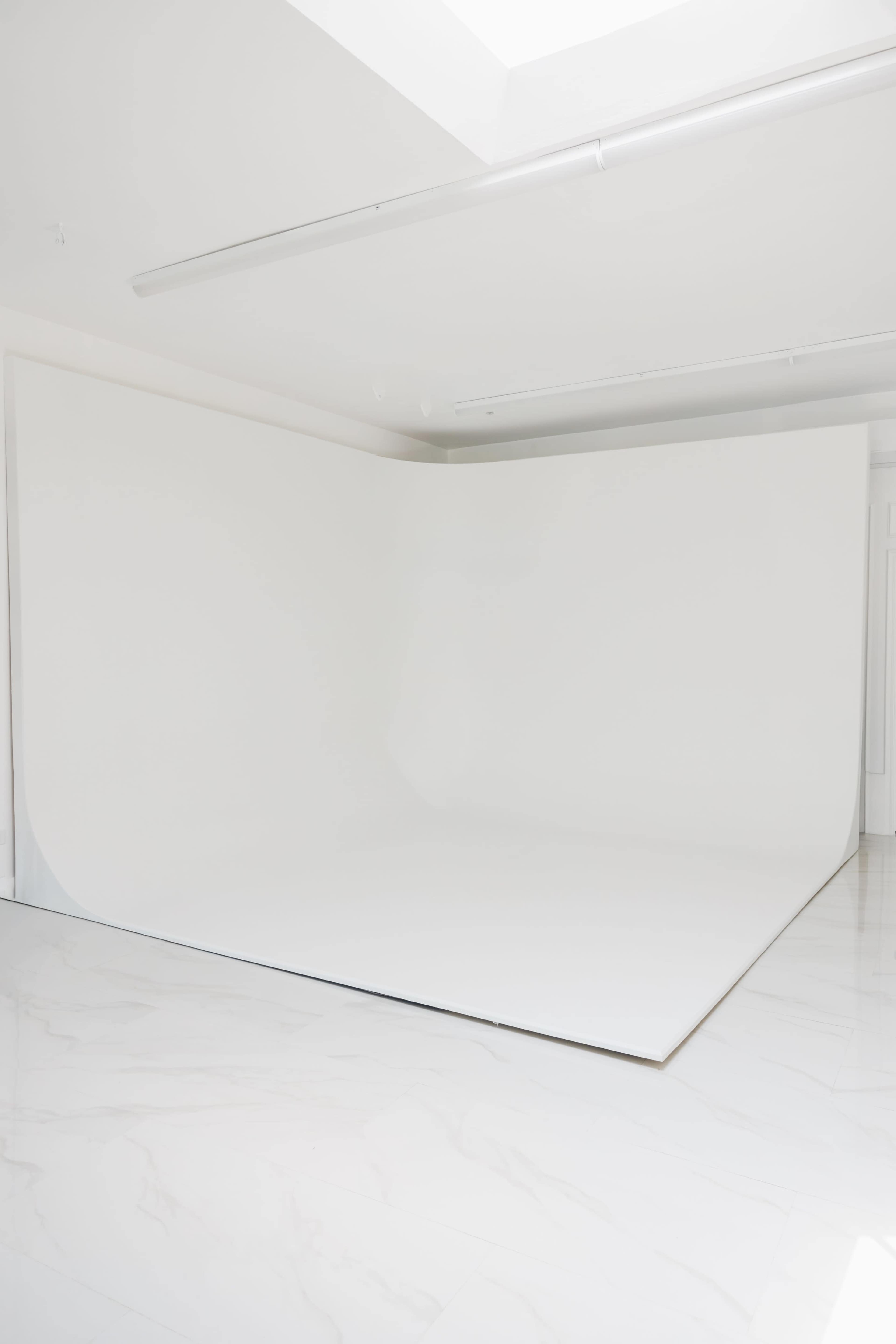 The image shows a minimalistic, well-lit studio space with a seamless white backdrop and a polished floor.