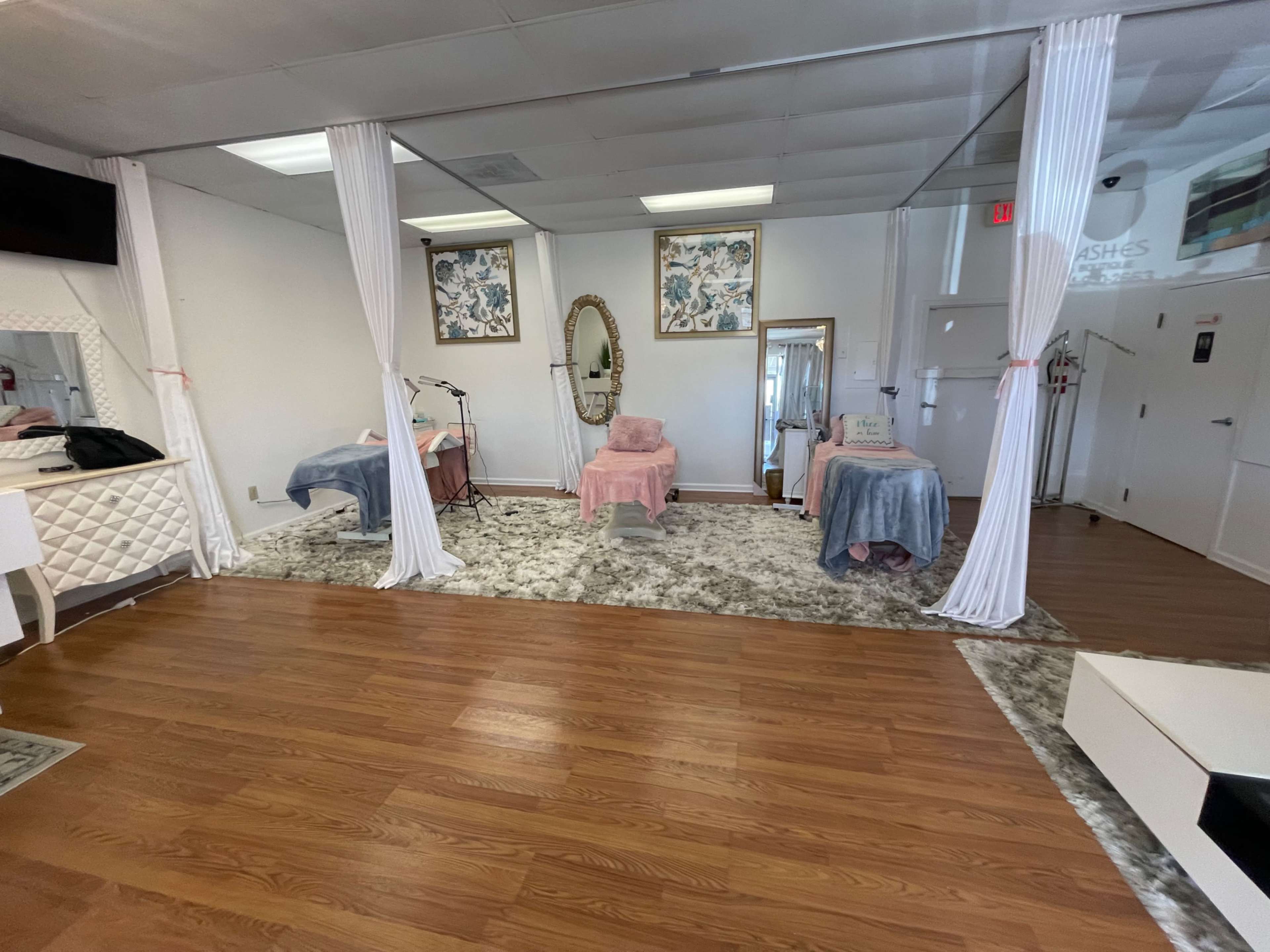 A salon interior with two treatment areas separated by white curtains, featuring a mirror, a chair, and decorative elements on the walls.