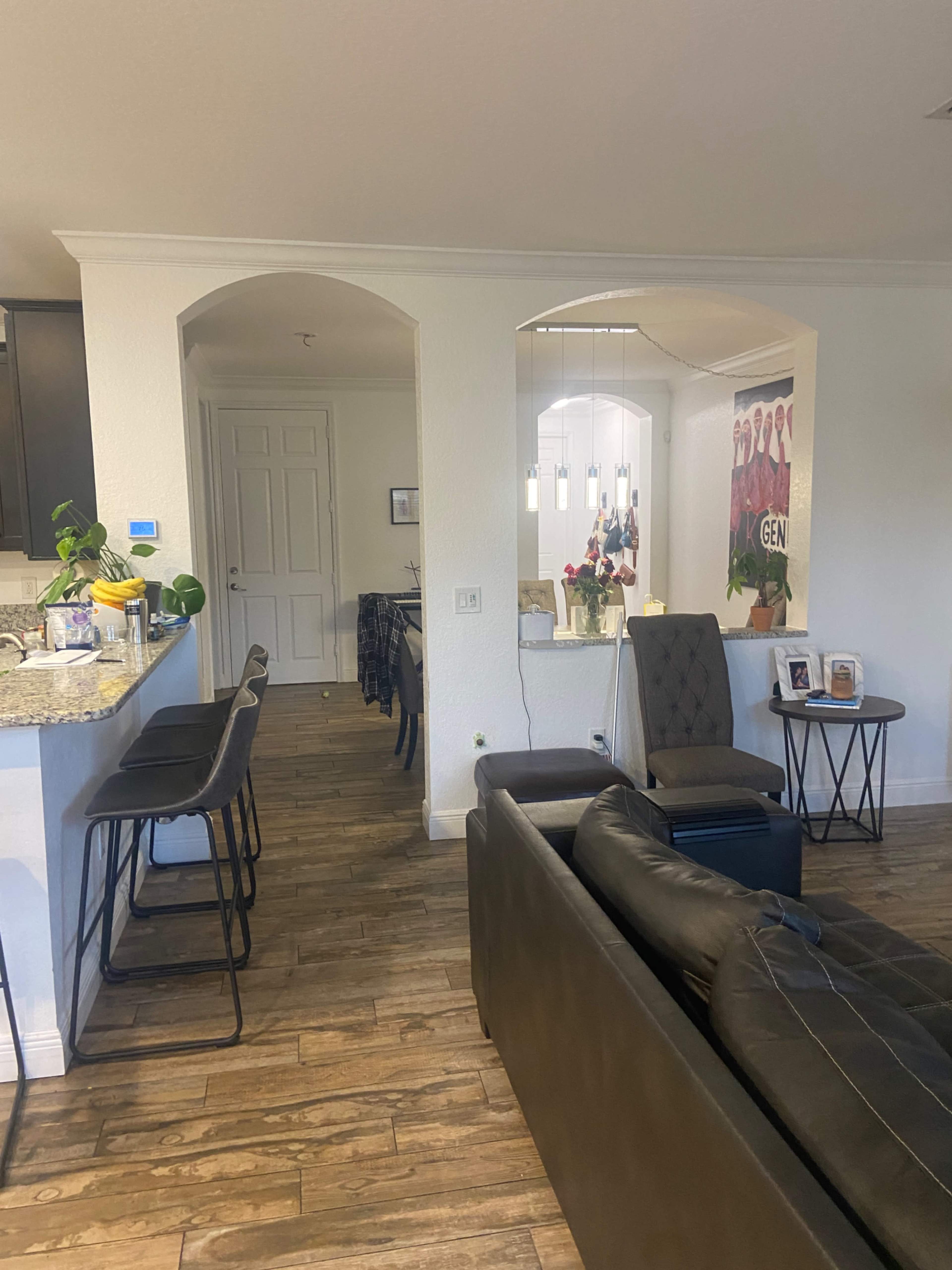 A living area with a sofa and bar stools opens into a dining area, featuring a table and decorative items.