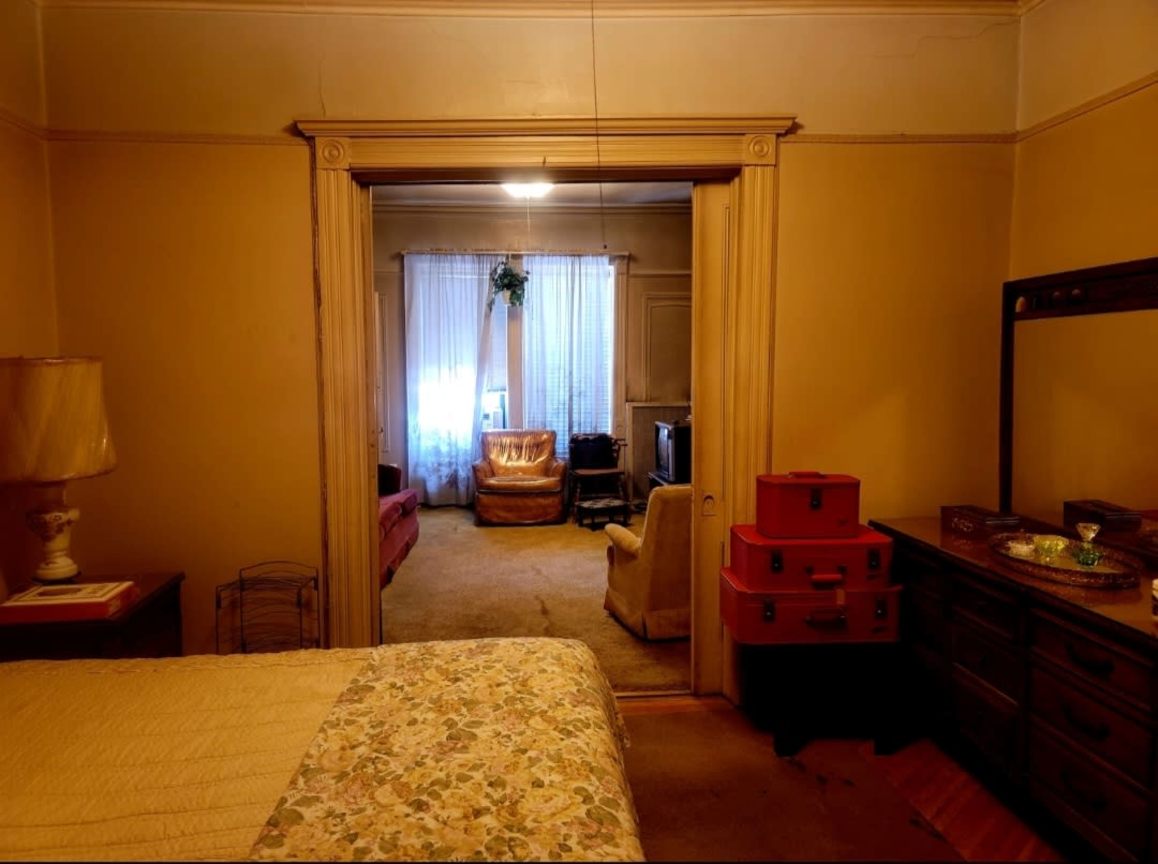 A view from a bedroom showing an adjoining living room with two sofas, a television, and natural light streaming through a window.