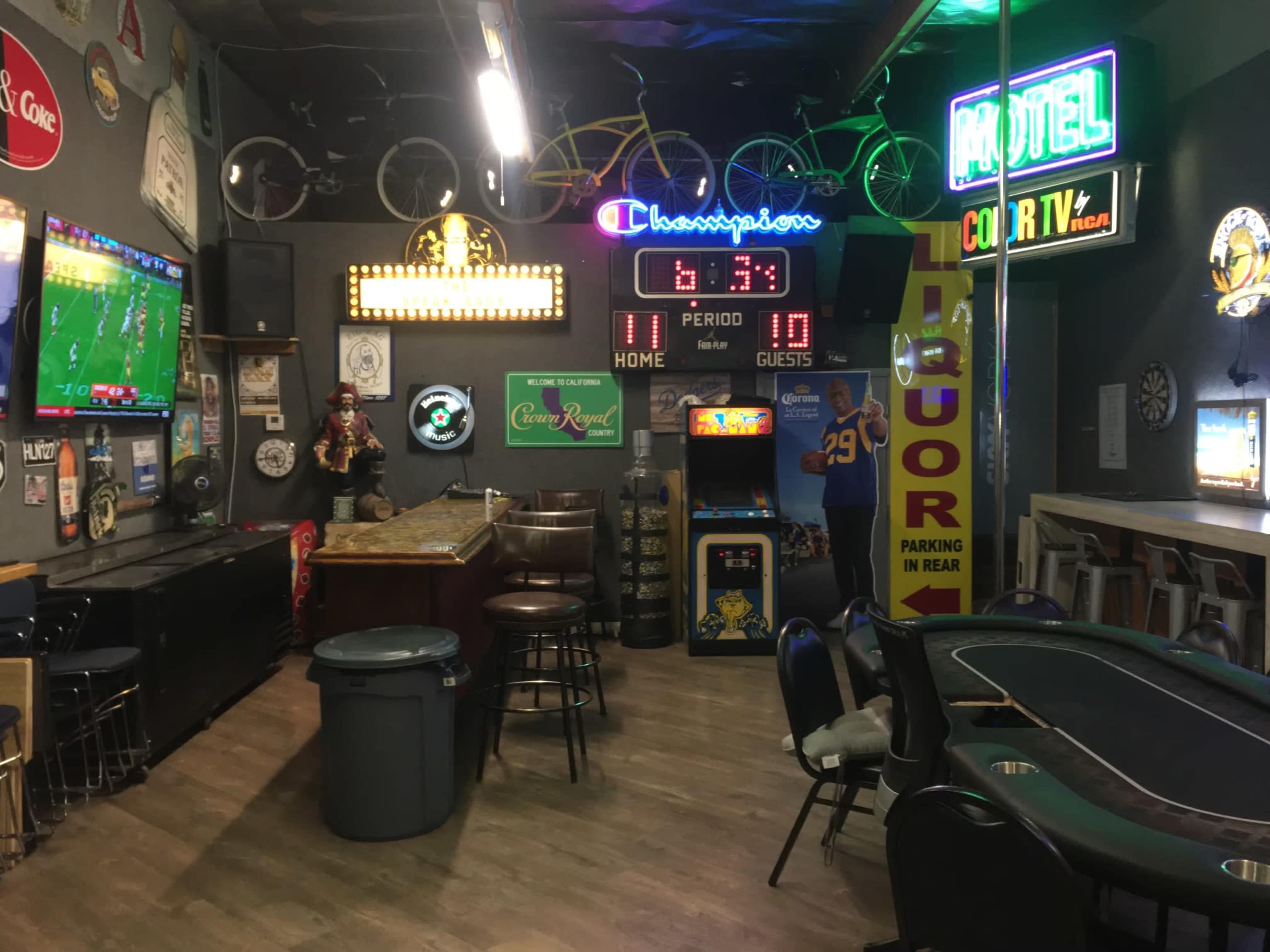 The interior of a lively bar or game room featuring neon signs, televisions displaying a sporting event, and various seating arrangements, including tables and chairs.