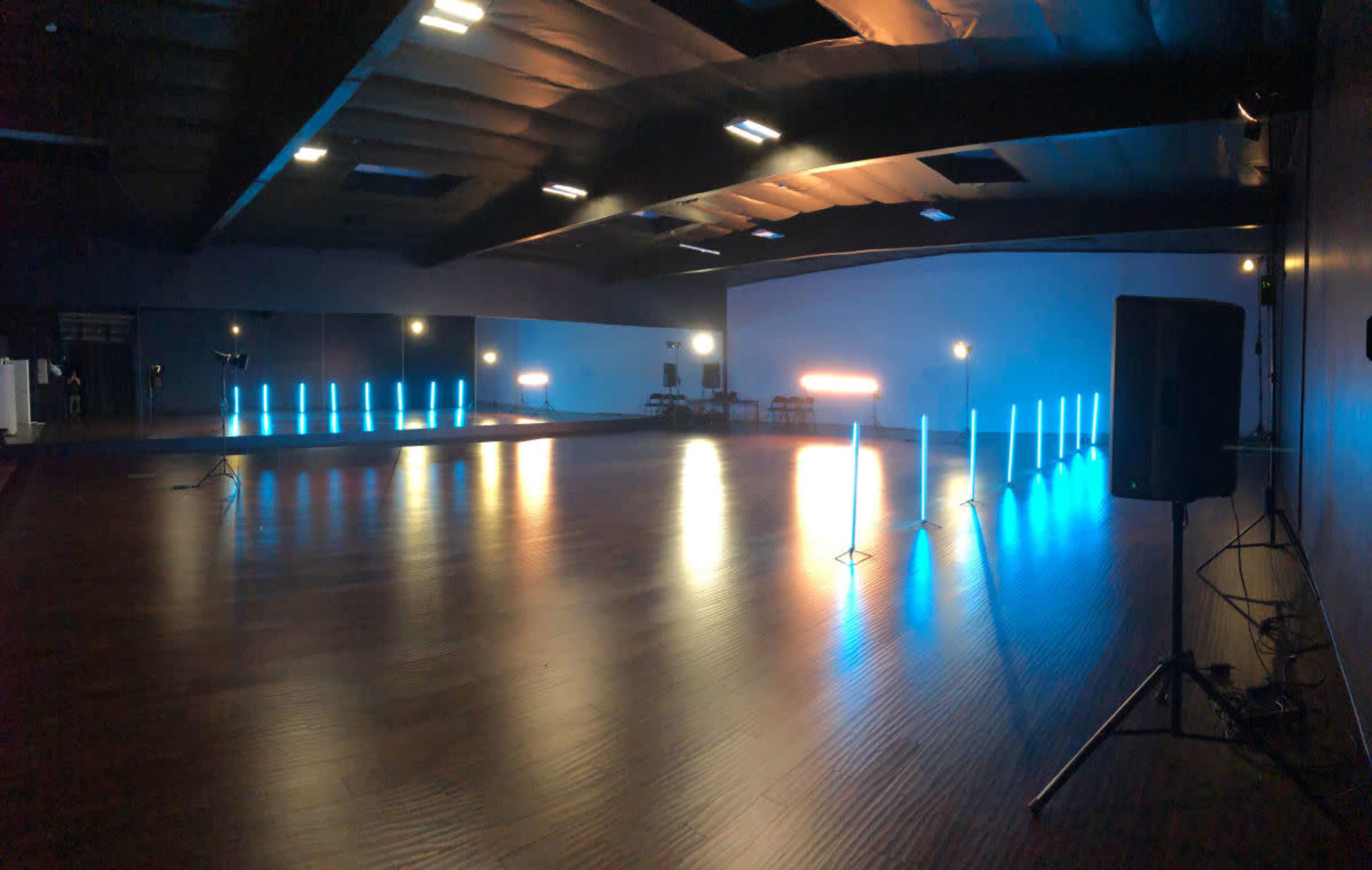 A spacious indoor event space with wooden flooring and illuminated vertical light fixtures in blue and white arranged around the area.