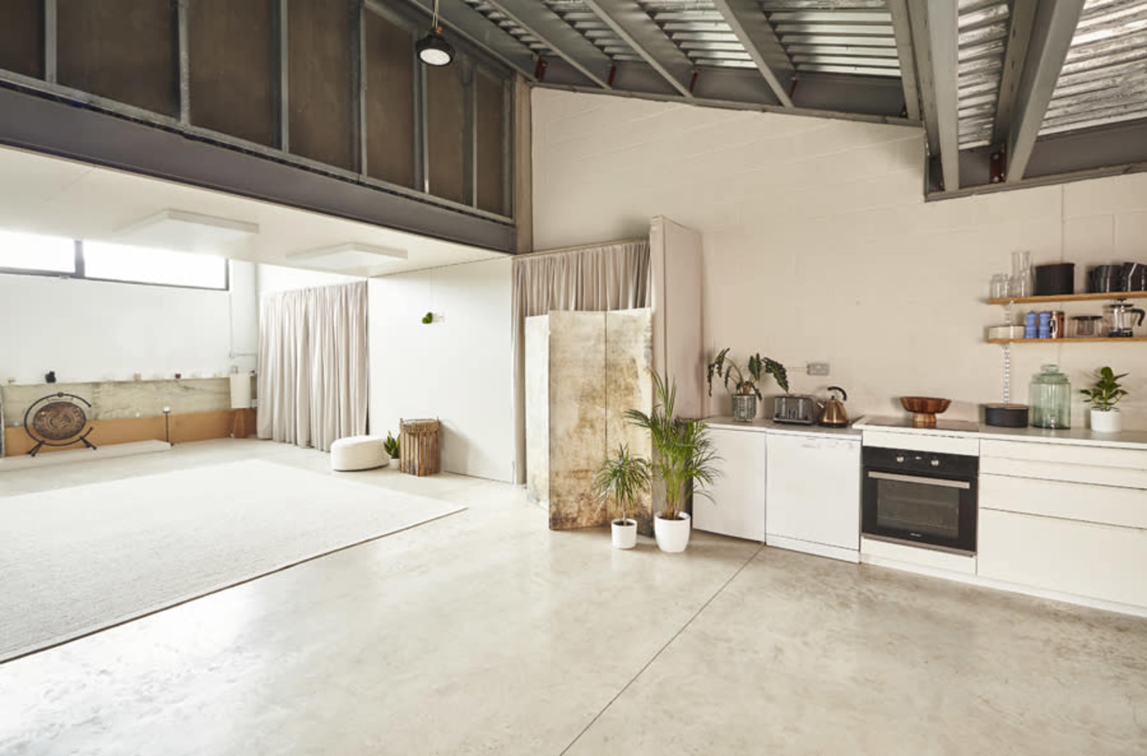 The image shows a spacious, modern interior with a minimalist kitchen, a large open area with a light-colored rug, and soft drapes separating different zones.