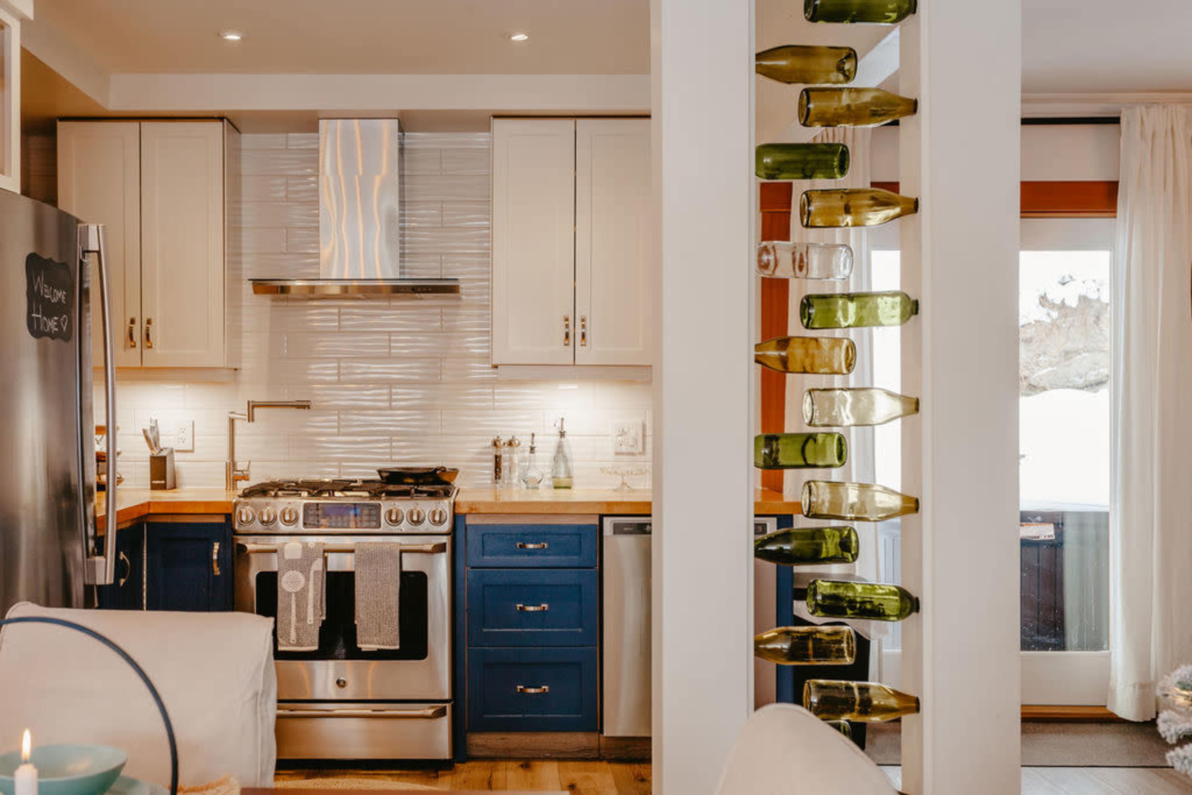 A modern kitchen with sleek cabinets, stainless steel appliances, and a decorative wine bottle display mounted on a column.