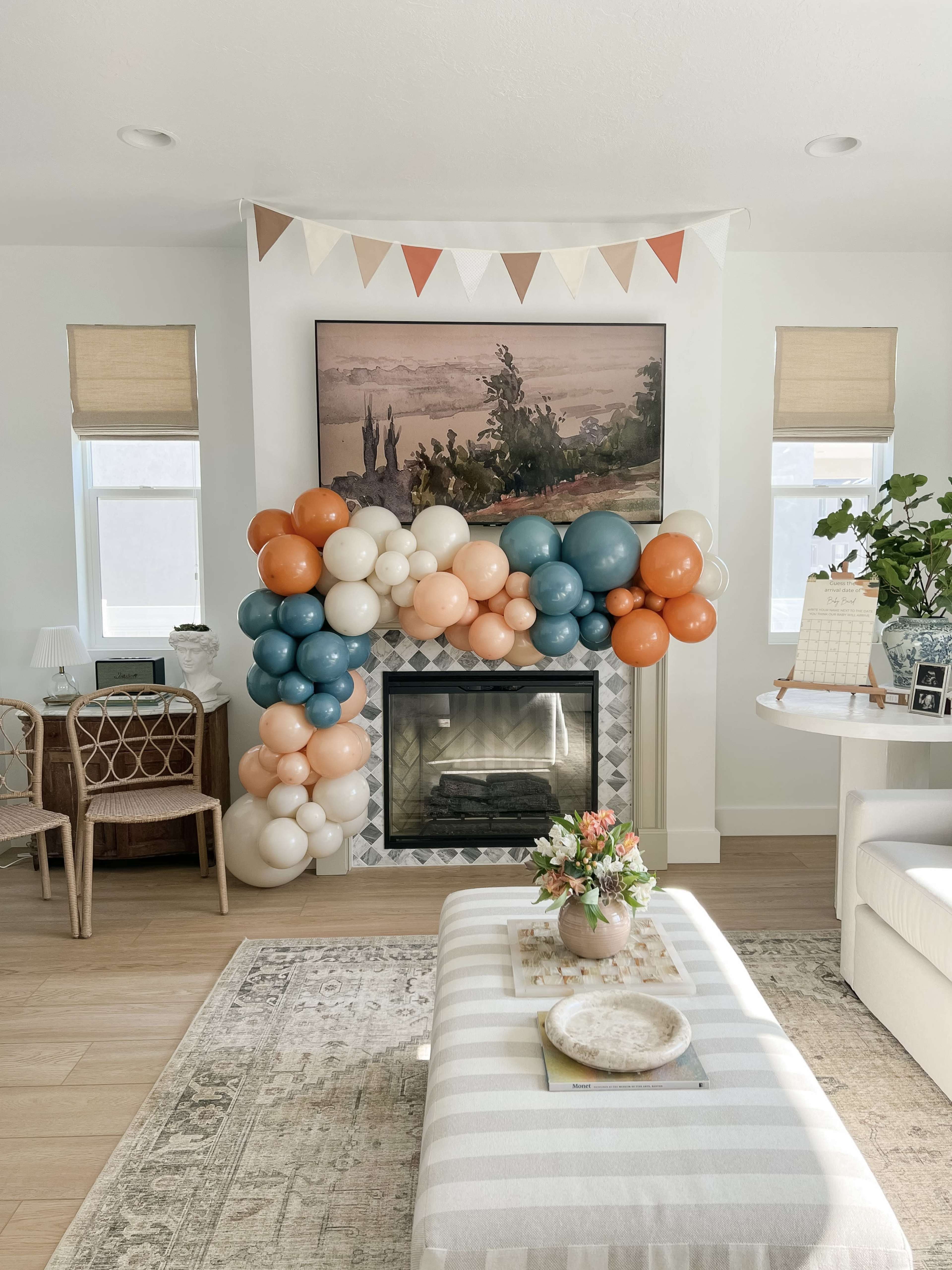The room features a decorated fireplace adorned with a large balloon garland in shades of blue, orange, and cream, with a small floral arrangement on a coffee table.